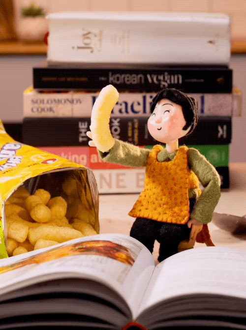Stop-motion puppet eating banana kick in front of a stack of cookbooks