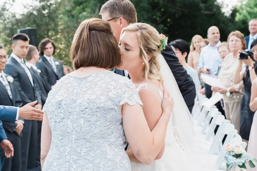 Bride kisses her mom at wedding ceremony.