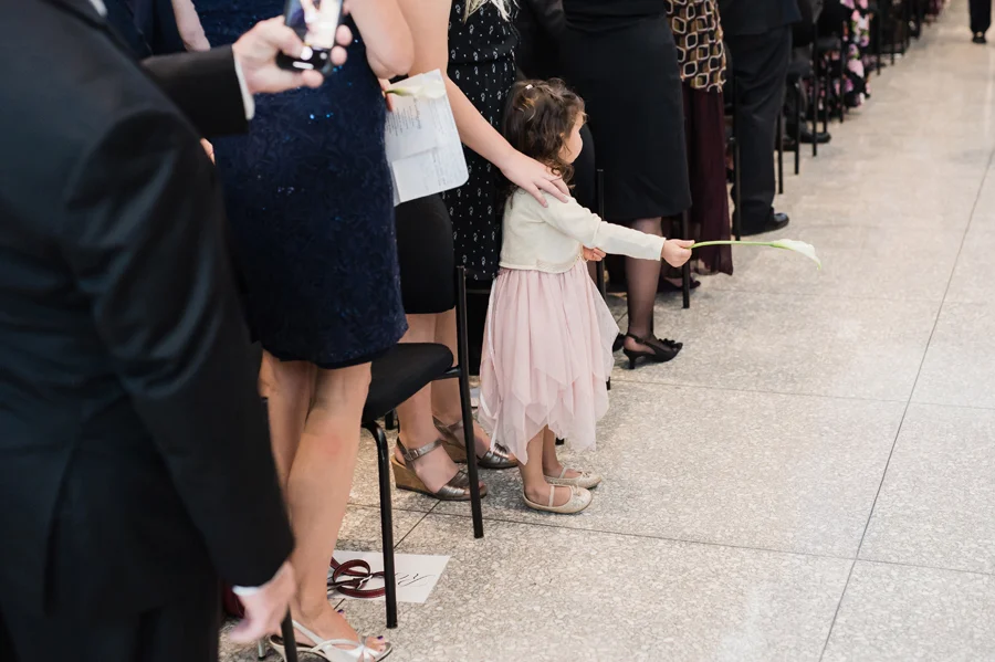 Girl holds flowers up for bride as she walks down the aisle.