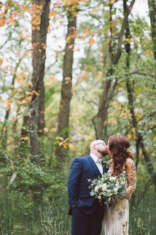 Bride and groom kiss in woods.