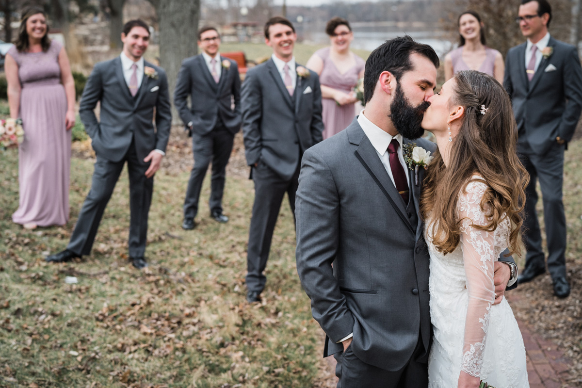 Bride and groom kiss with the bridal party in the background.