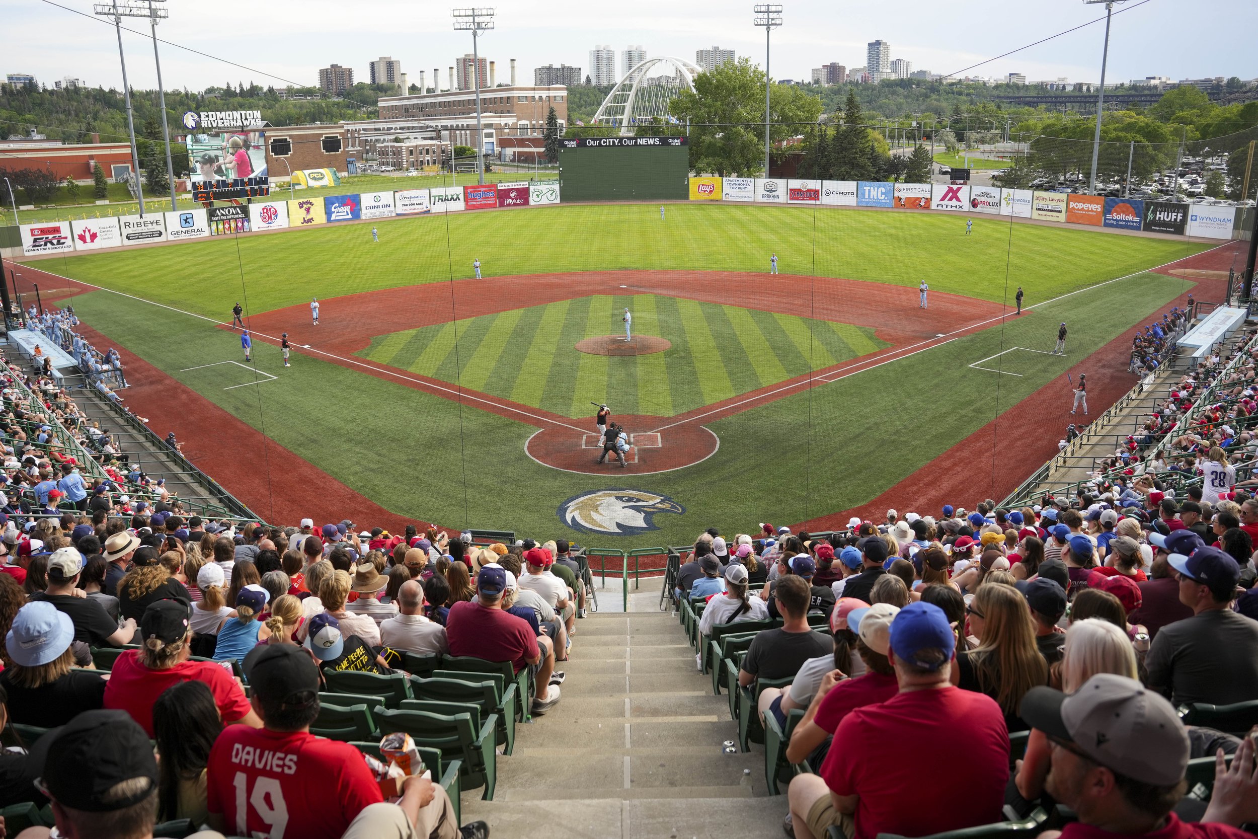 A view of a baseball stadium filled with spectators, with players on the field and city buildings in the background.