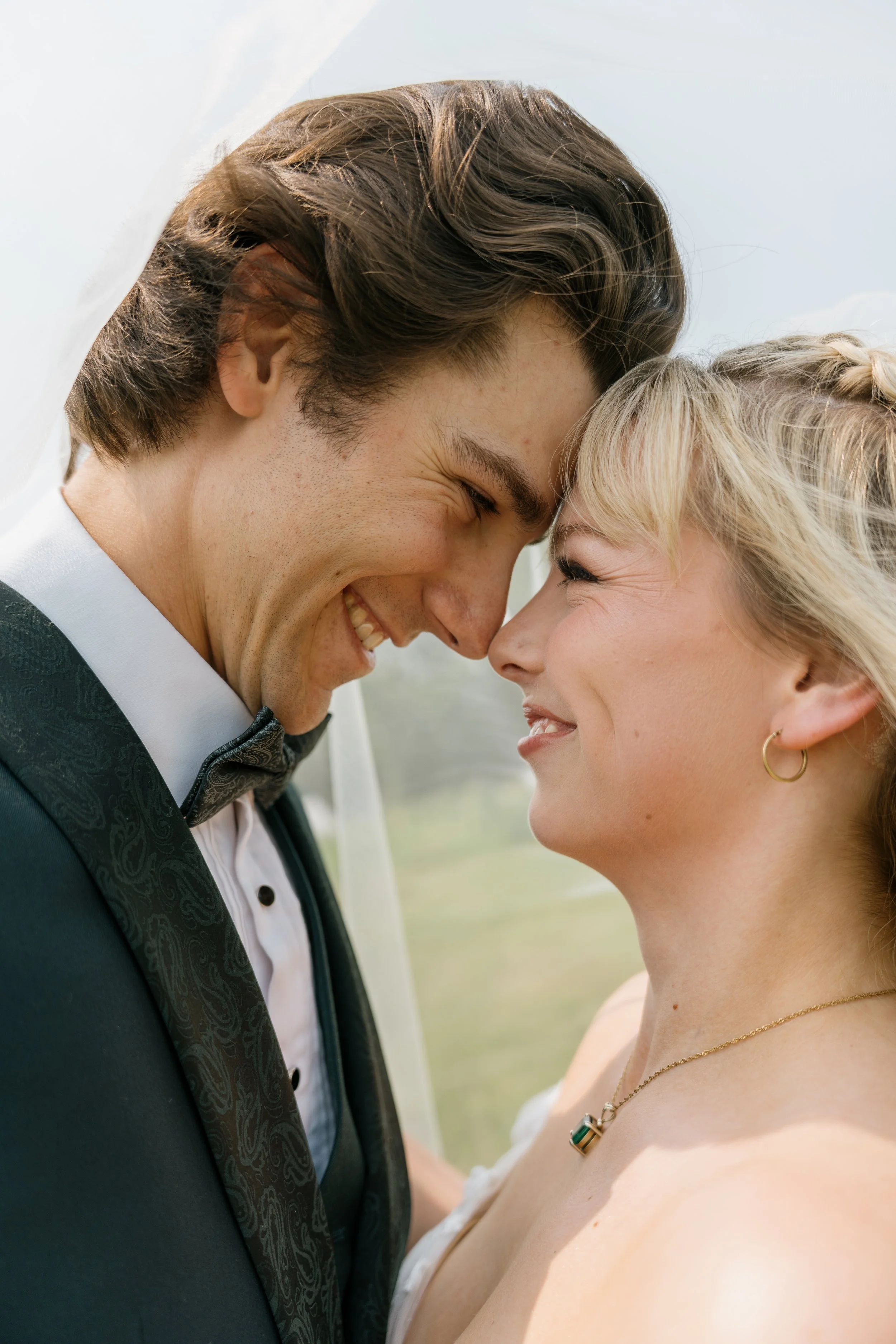 A happy bride and groom with their foreheads touching, smiling at each other during a wedding ceremony.