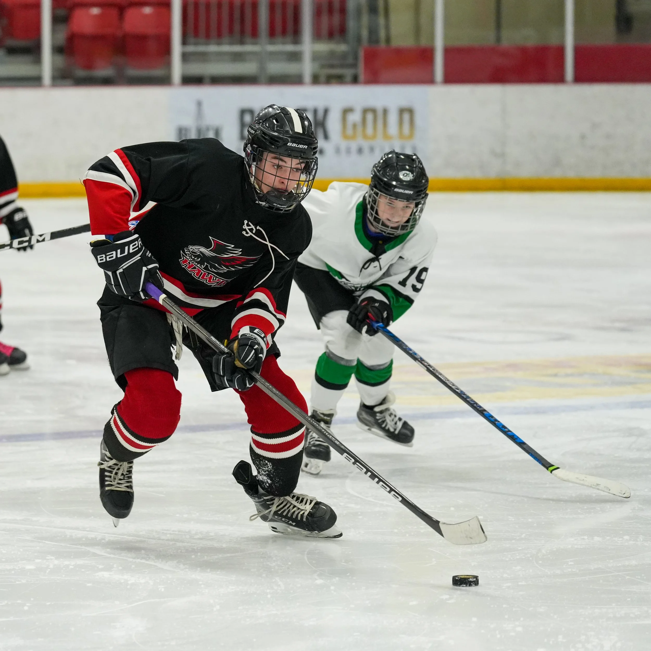 Ice hockey players fighting for the puck on the ice rink, wearing helmets and jerseys.
