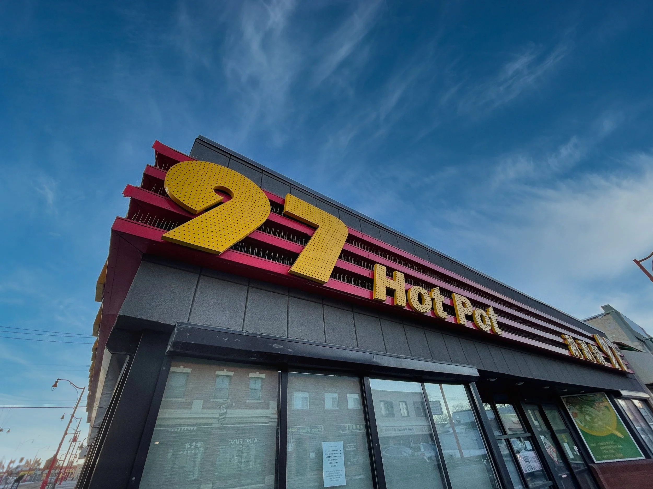 Looking up at a building with large yellow letters spelling '24' on the top corner, under a partly cloudy sky.
