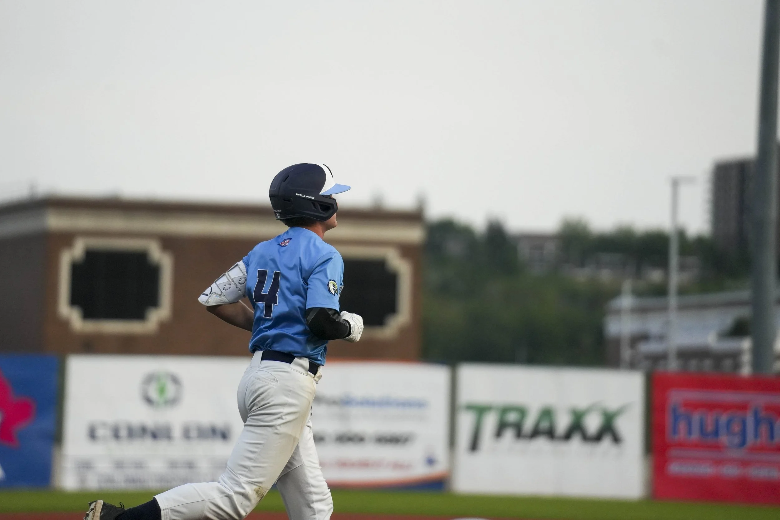 A baseball player wearing a blue uniform and helmet, running on the field during a game, with blurred advertisements and structures in the background.