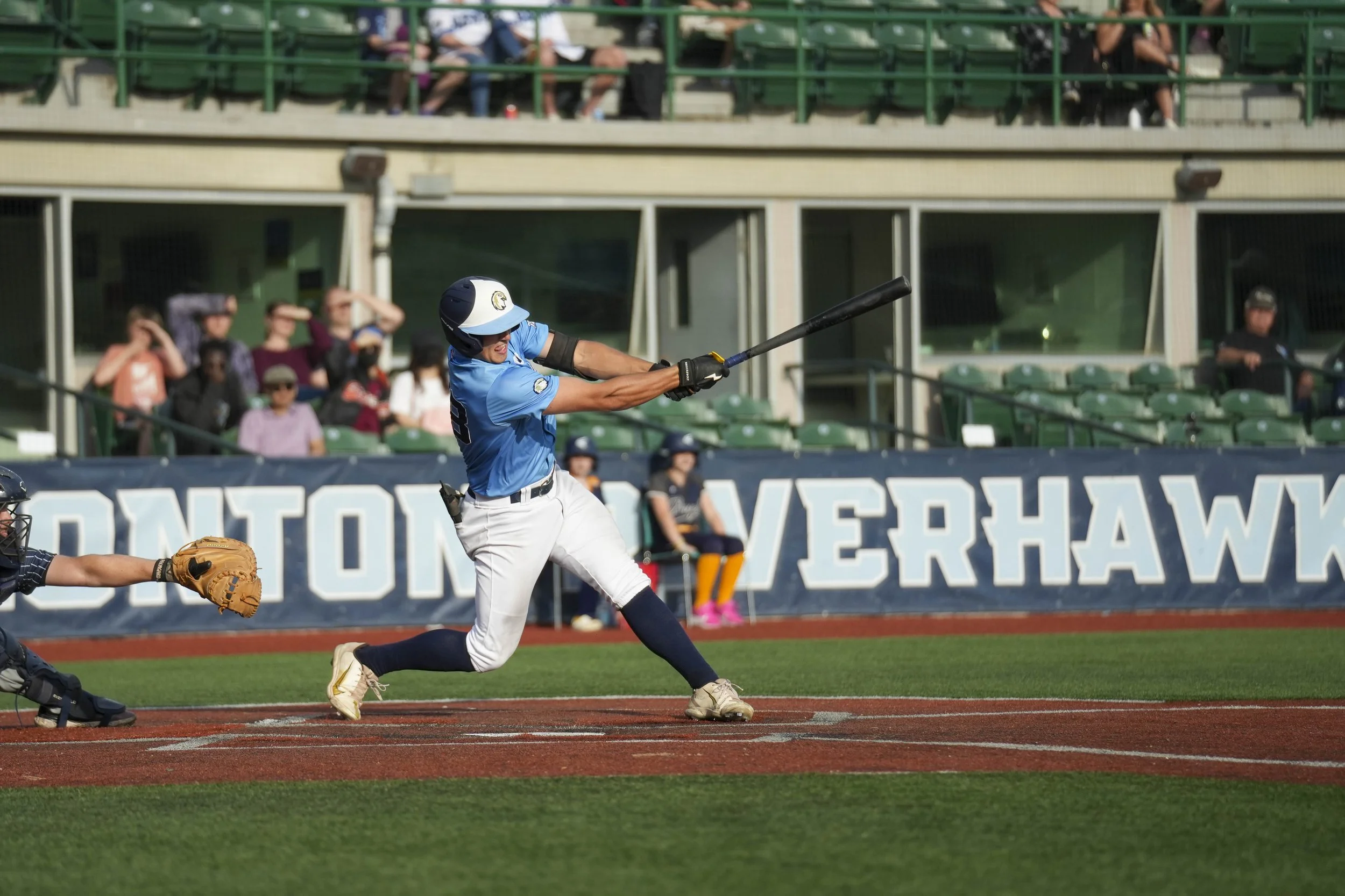 A baseball player in a blue jersey and white pants is swinging a bat during a game at a stadium with spectators in the stands.