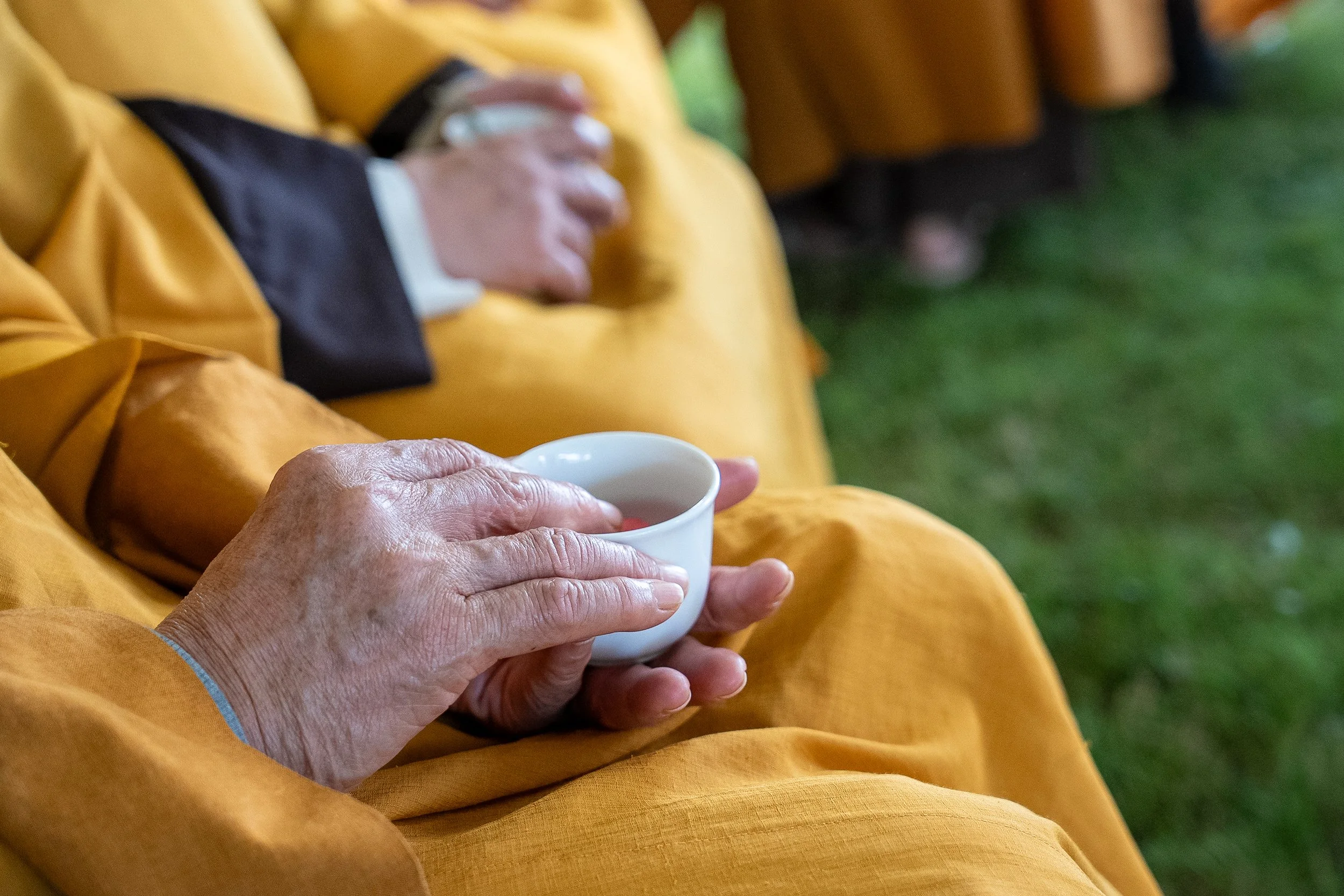 Close-up of a person in a yellow coat holding a white cup, with other people in yellow coats blurred in the background.
