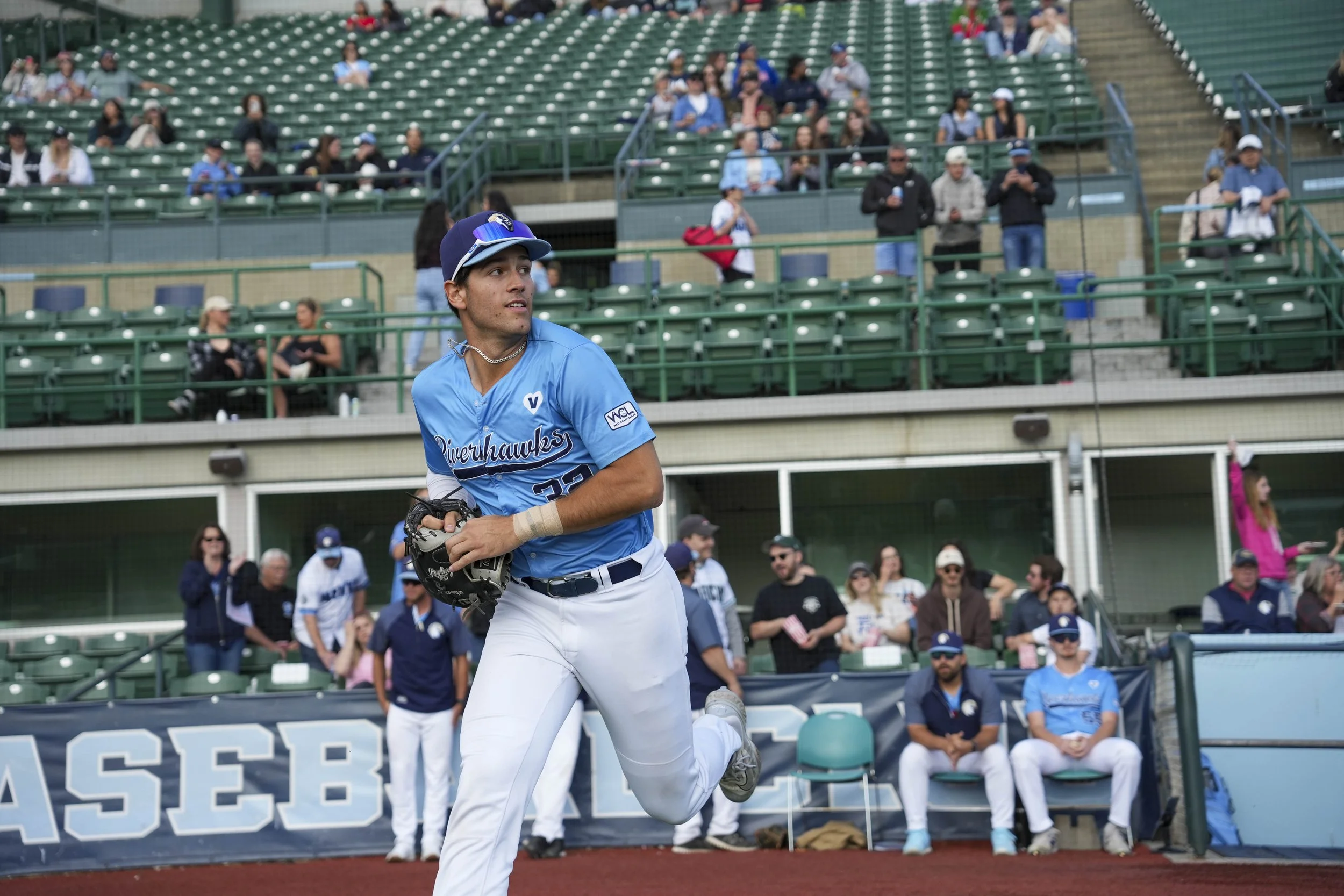 A male baseball player in a blue jersey and white pants running on the field with spectators sitting in the stands behind him.