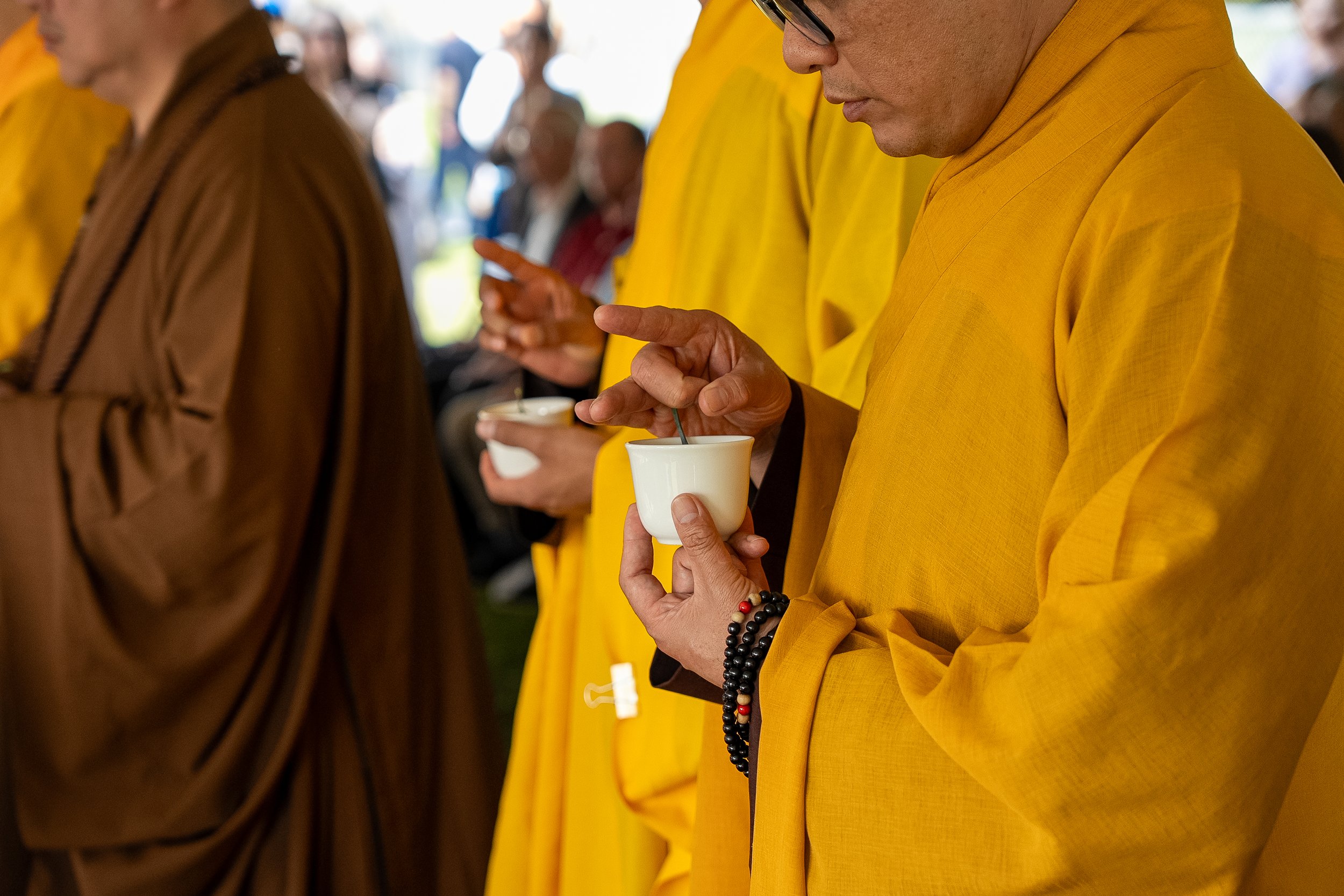 Close-up of a person wearing a yellow garment holding a cup, with another person in brown clothing beside them, at a gathering or event.