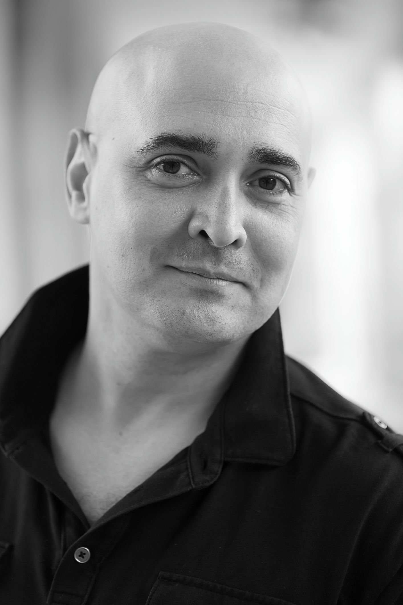Close-up portrait of a woman with dark brown, textured dreadlocks, light makeup, and wearing a dark green top, against a neutral background.