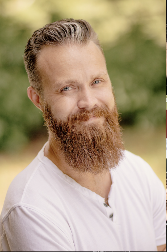 A woman with a buzz cut hairstyle, blue eyes, wearing earrings and a pink sleeveless top, looking directly at the camera with a neutral expression.