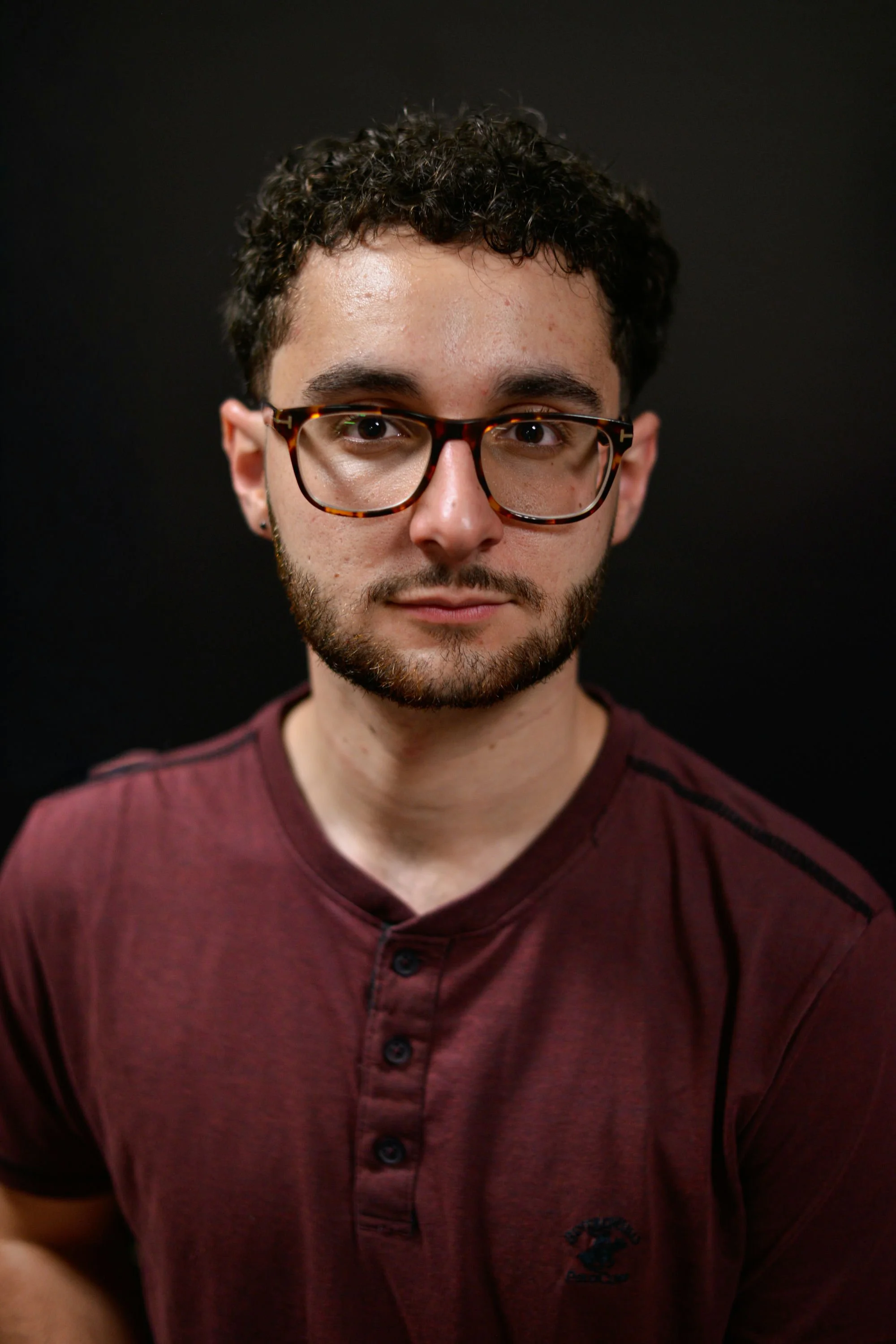 A woman with braided hair, wearing a blue sleeveless top, jewelry including earrings and necklaces, in an outdoor setting with blurred trees and grass in the background.
