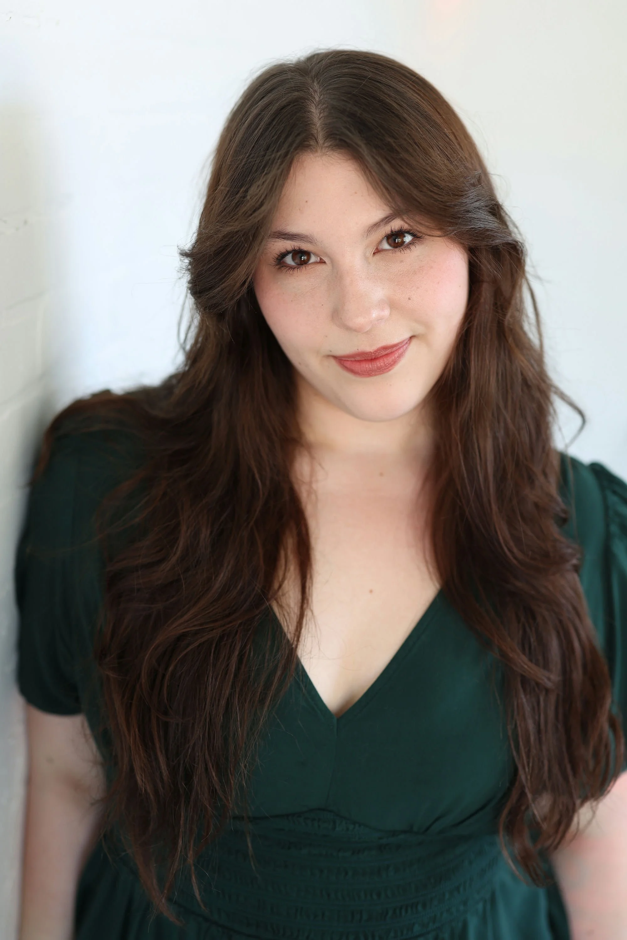 Portrait of a young woman with long blonde hair, smiling, outdoors with trees and sunlight in the background.