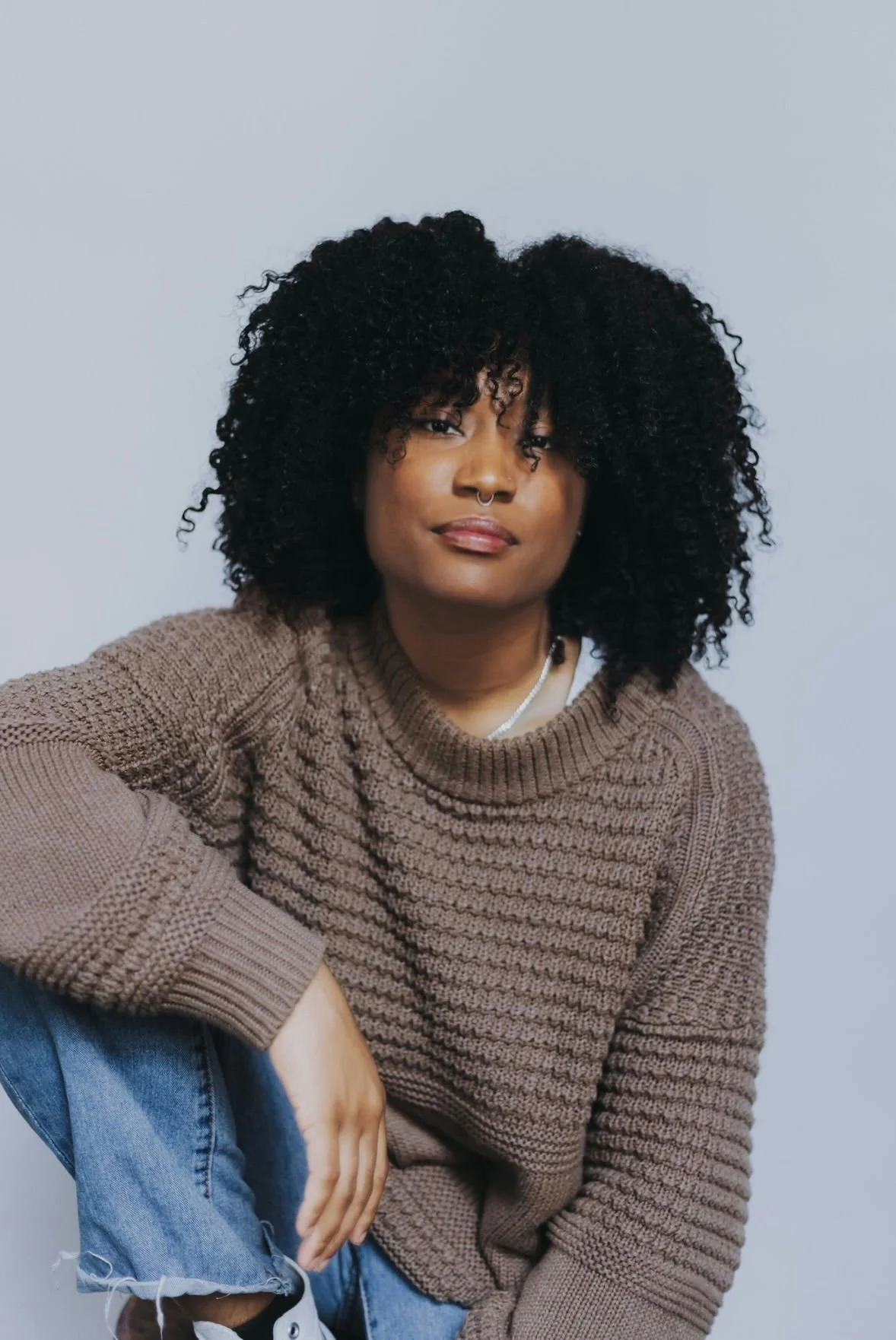 A woman with a buzz cut hairstyle, blue eyes, wearing earrings and a pink sleeveless top, looking directly at the camera with a neutral expression.