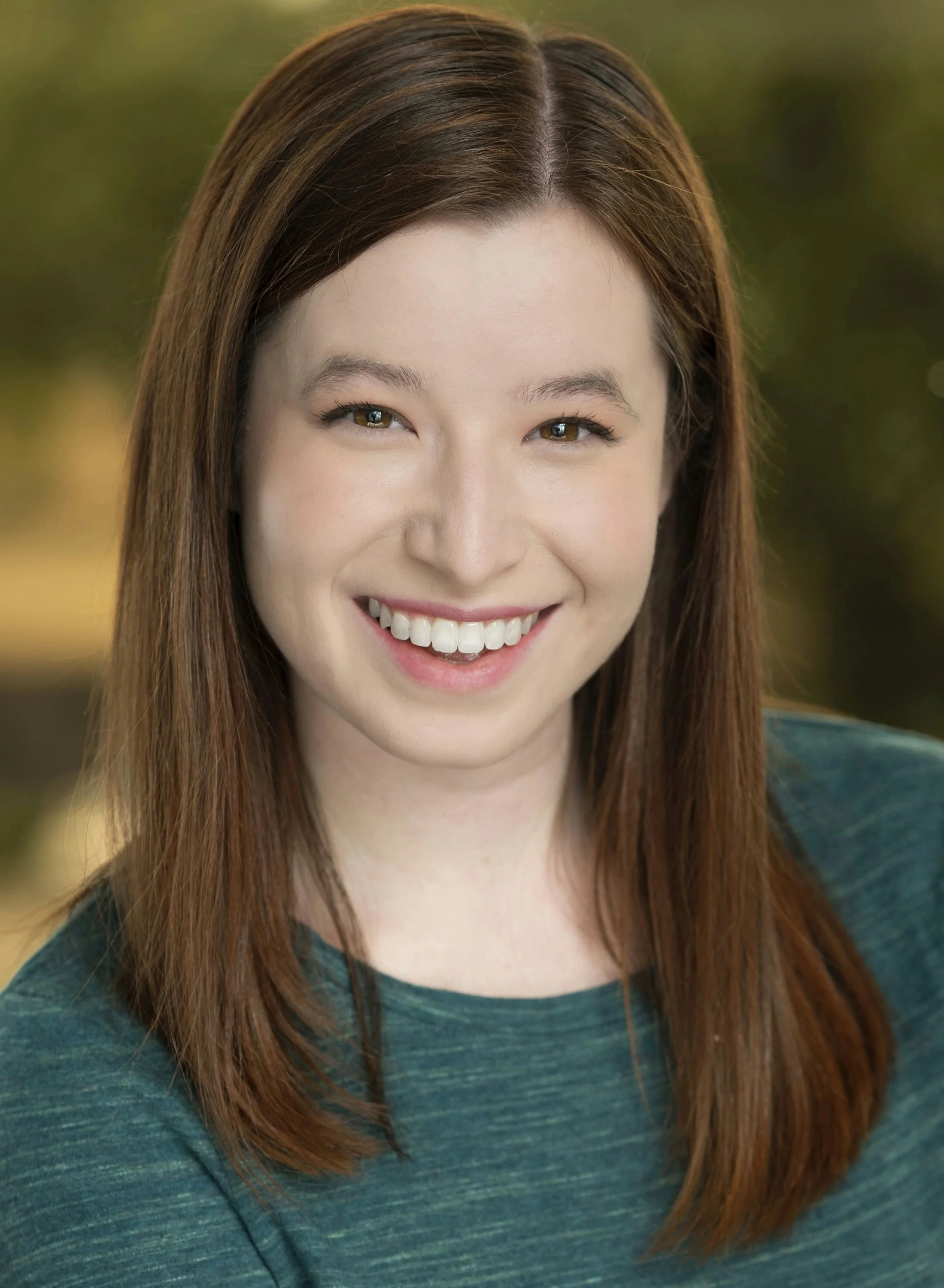 A woman with curly red hair wearing a sleeveless red top, looking at the camera with a slight smile.