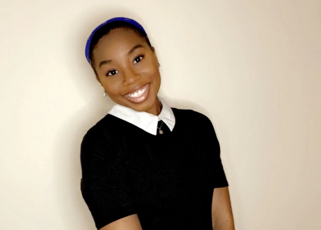 A smiling woman with dark curly hair, wearing hoop earrings and a cream-colored sweater, against a dark background.