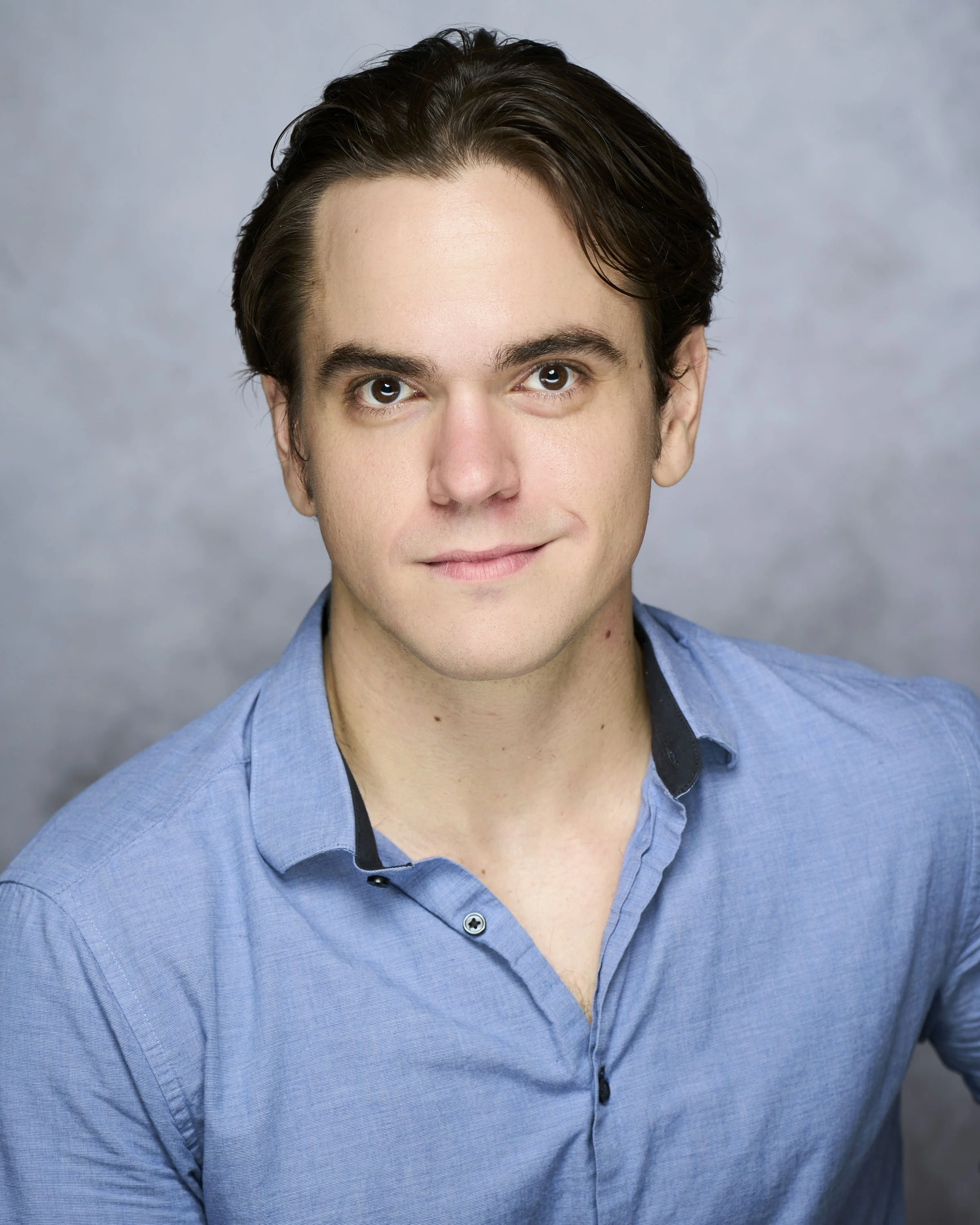 A woman with a buzz cut hairstyle, blue eyes, wearing earrings and a pink sleeveless top, looking directly at the camera with a neutral expression.