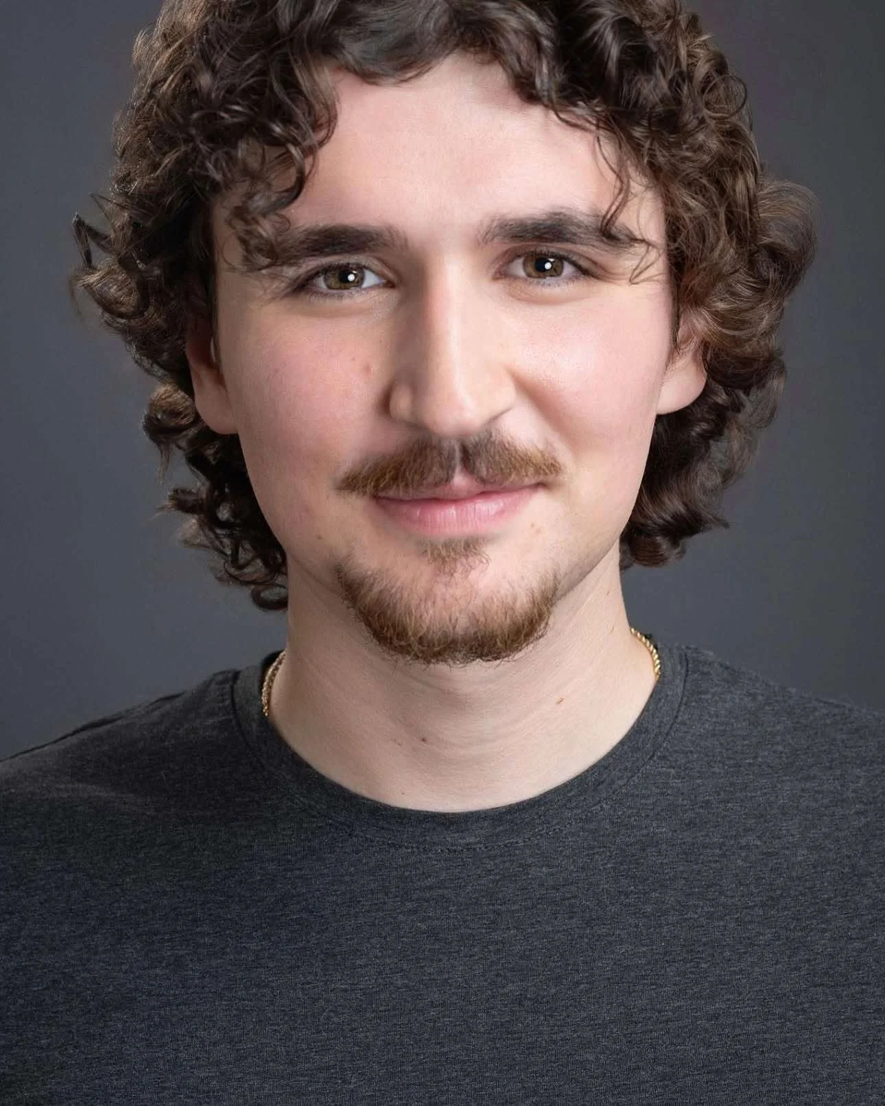 Close-up portrait of a woman with dark brown, textured dreadlocks, light makeup, and wearing a dark green top, against a neutral background.