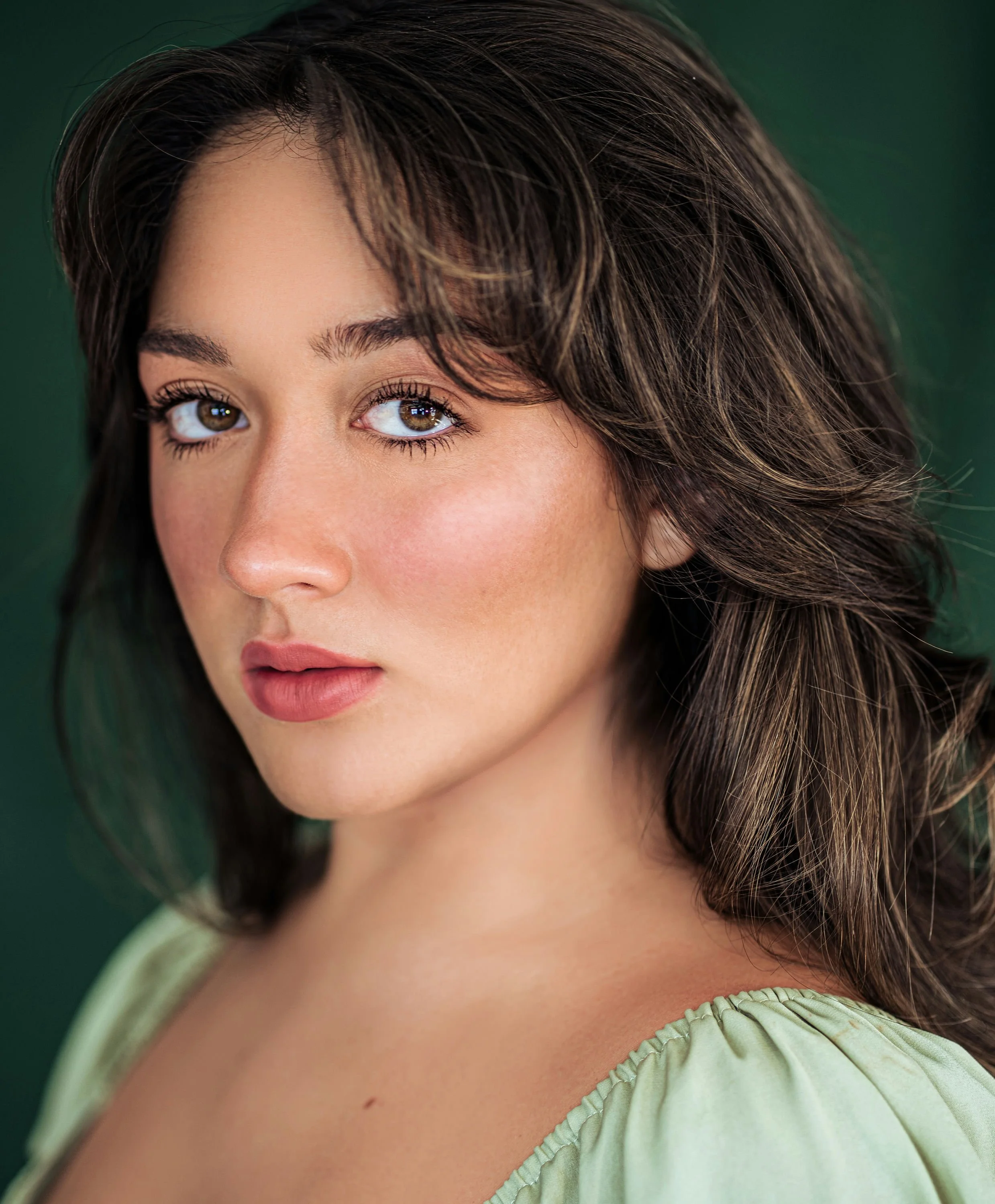 A woman with curly red hair wearing a sleeveless red top, looking at the camera with a slight smile.