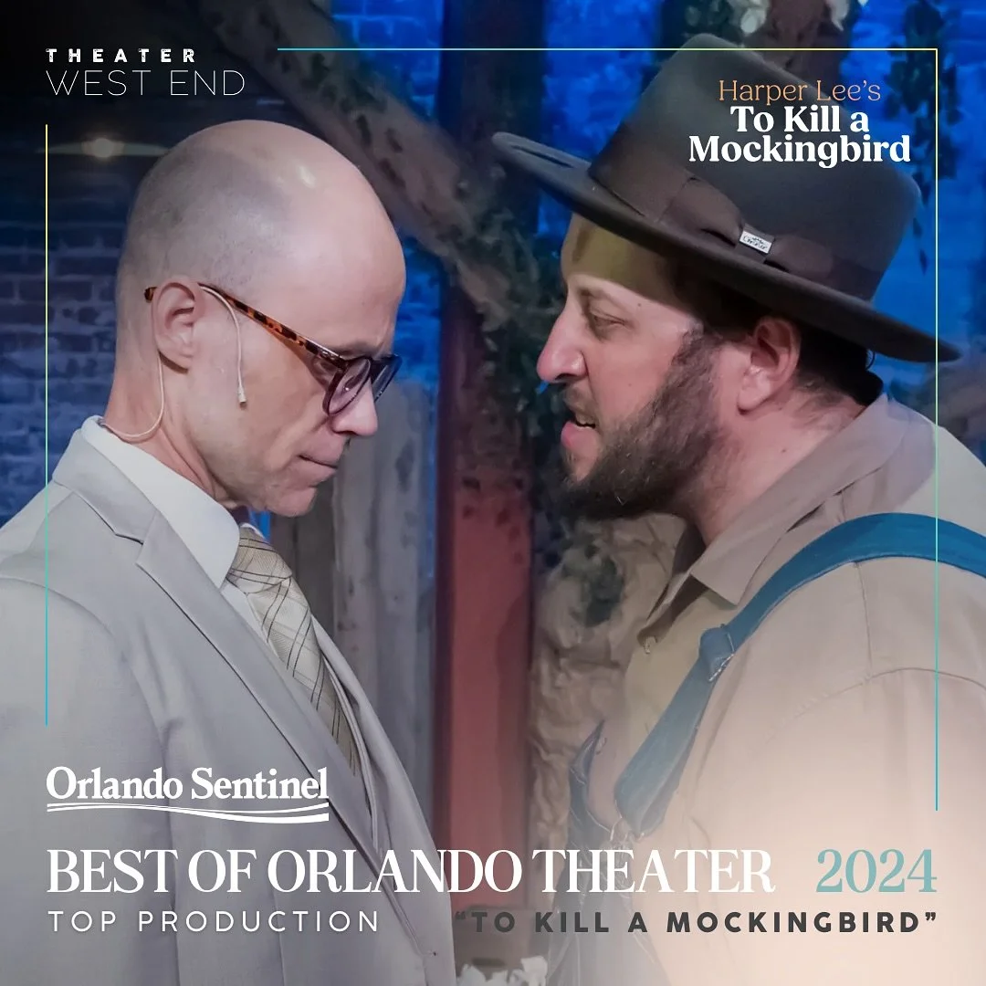 Two men on stage in a scene from 'To Kill a Mockingbird.' One is bald with glasses, wearing a light-colored suit and tie, looking downward. The other has a beard, is wearing a wide-brimmed hat and tan sheriff-style uniform, looking at the first man. The background features a tree and stage lighting.