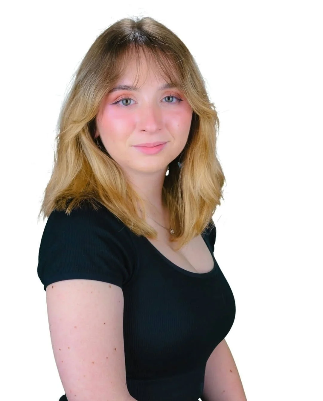 A young woman with shoulder-length wavy blonde hair, wearing a black top, smiling softly against a white background.