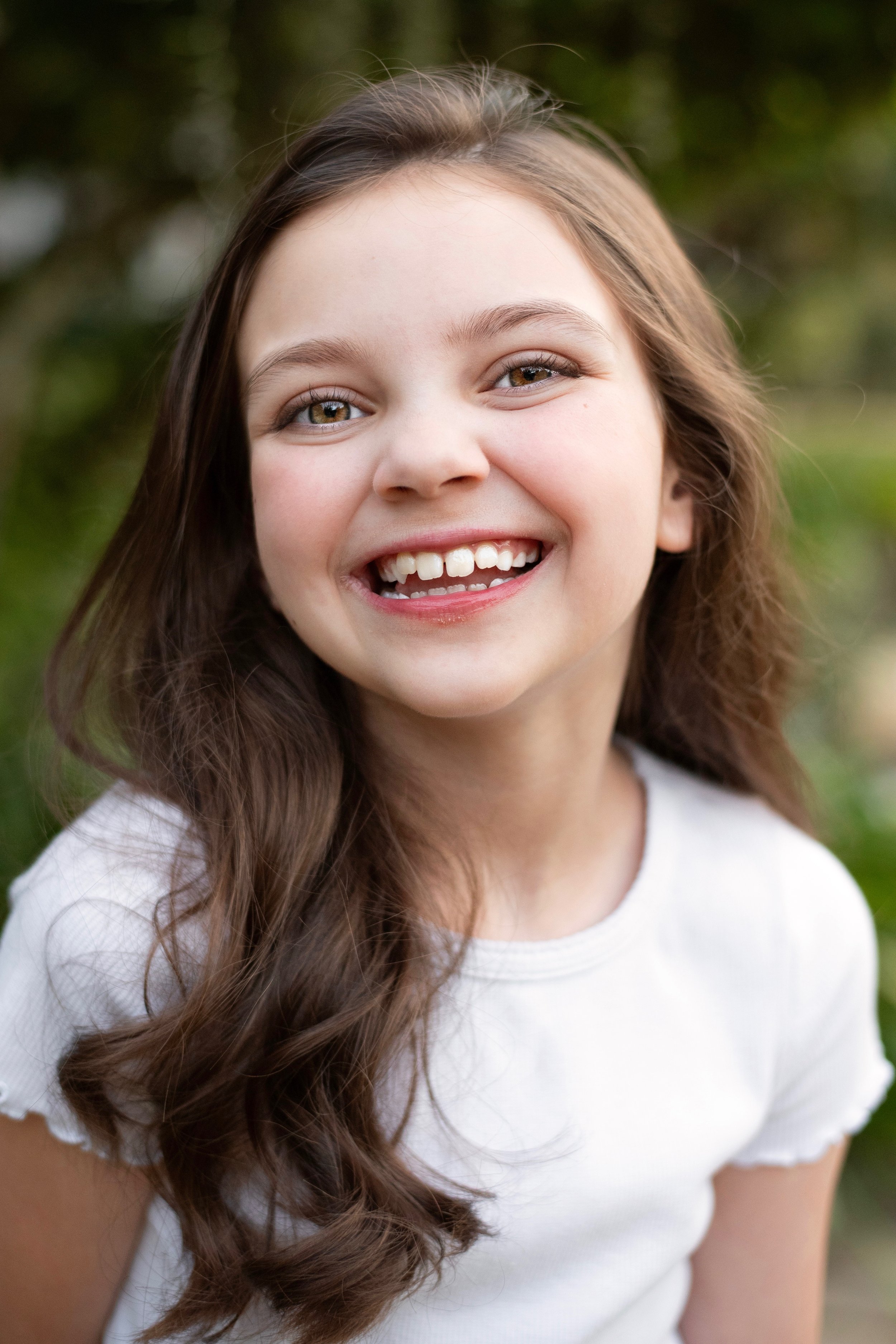 A woman with short, wavy brown hair, wearing a green blouse with a subtle polka dot pattern, smiling softly against a dark, blurred background.