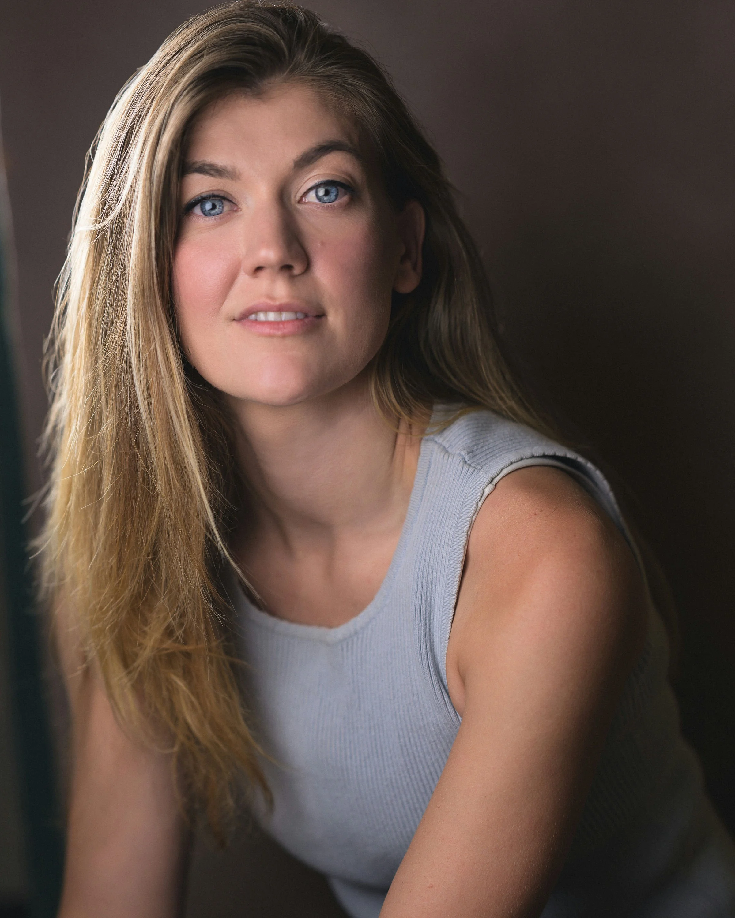 A woman with curly red hair wearing a sleeveless red top, looking at the camera with a slight smile.