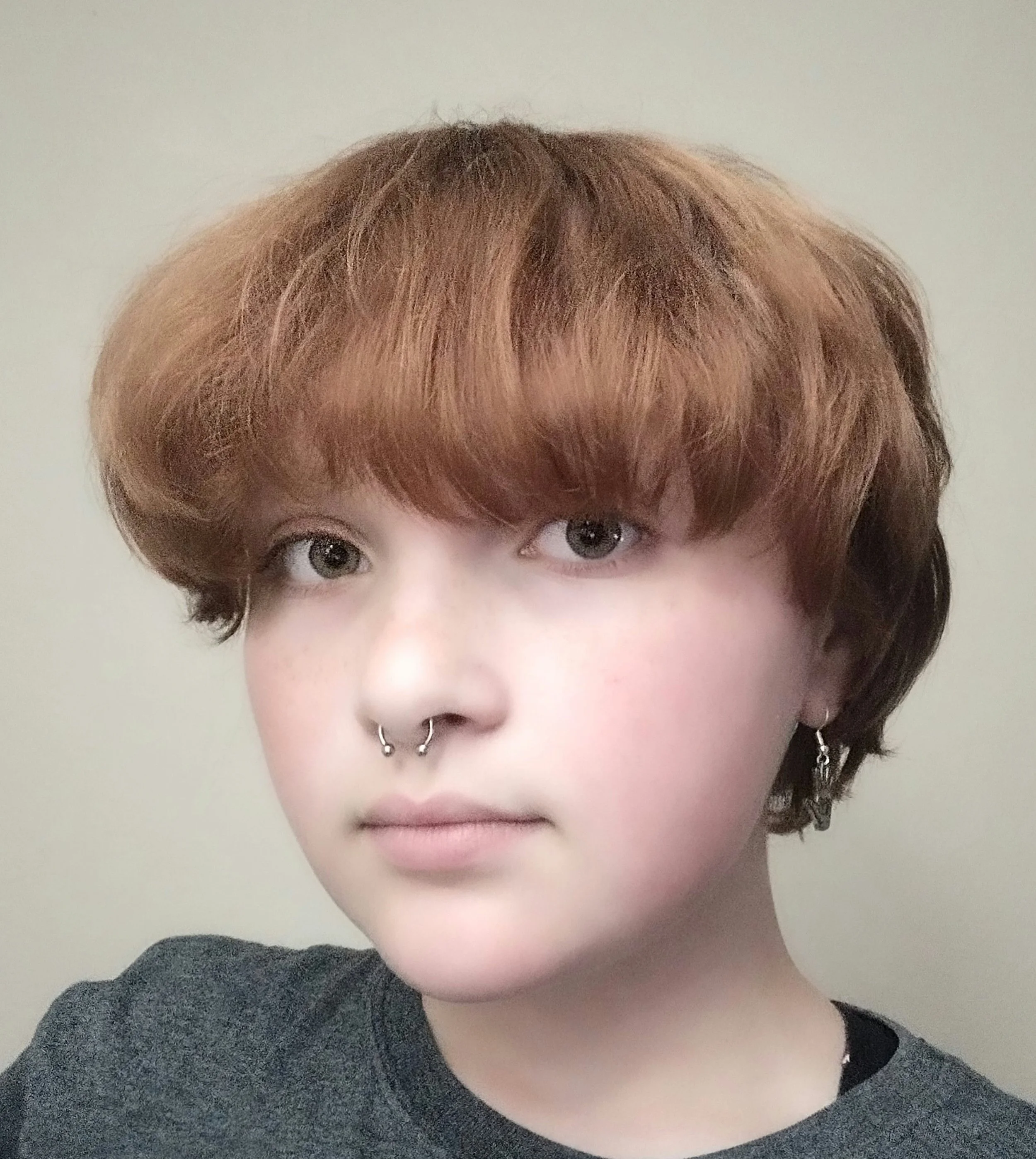 Portrait of a young woman with red wavy hair and blue eyes, wearing a dark blue blouse, standing against a blue background.