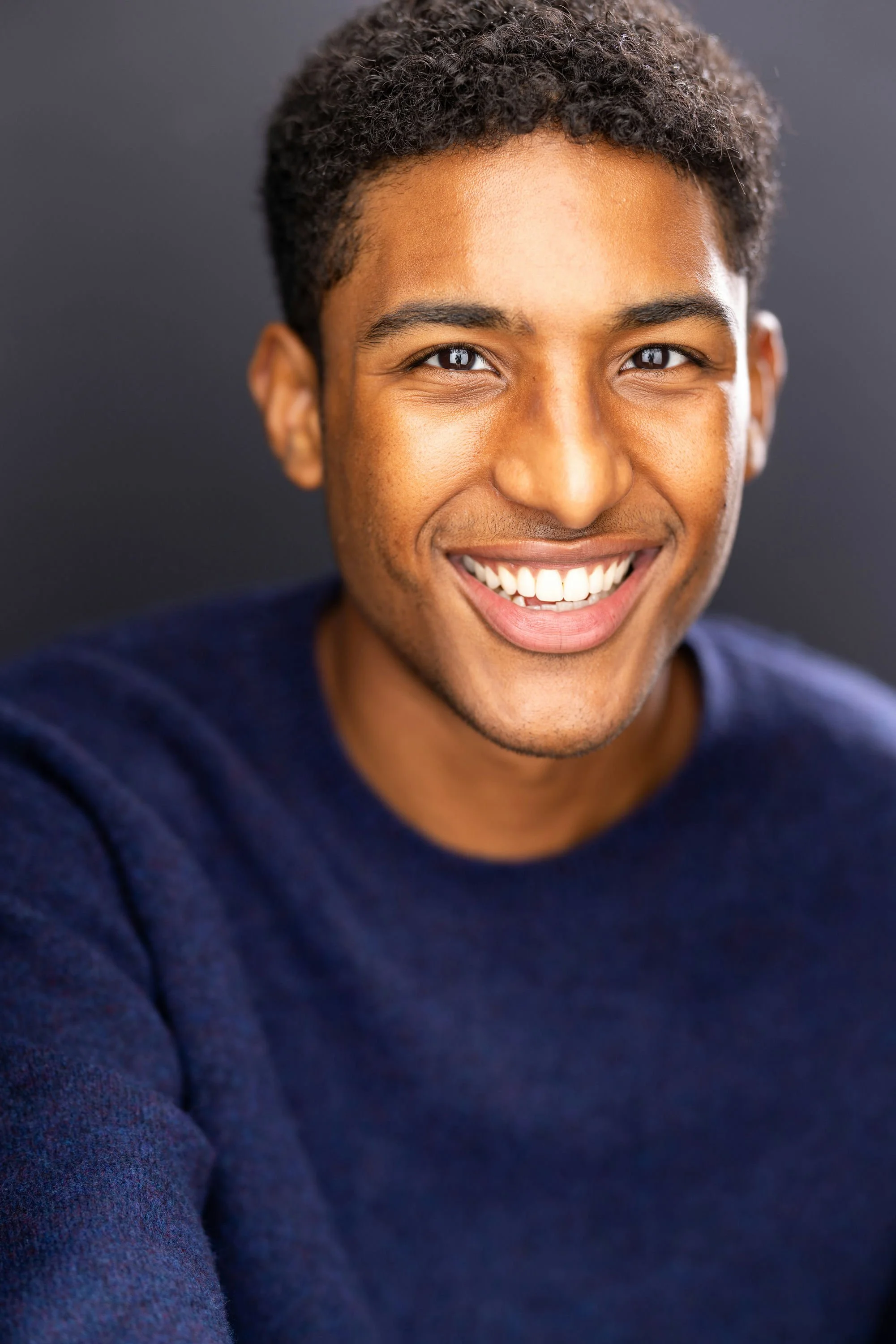 A woman with short, wavy brown hair, wearing a green blouse with a subtle polka dot pattern, smiling softly against a dark, blurred background.