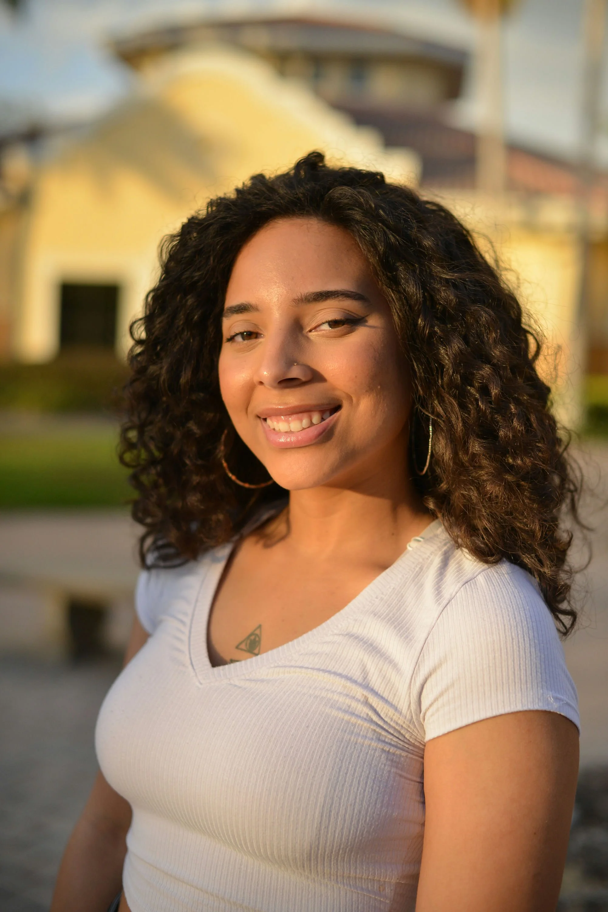 A woman with a buzz cut hairstyle, blue eyes, wearing earrings and a pink sleeveless top, looking directly at the camera with a neutral expression.