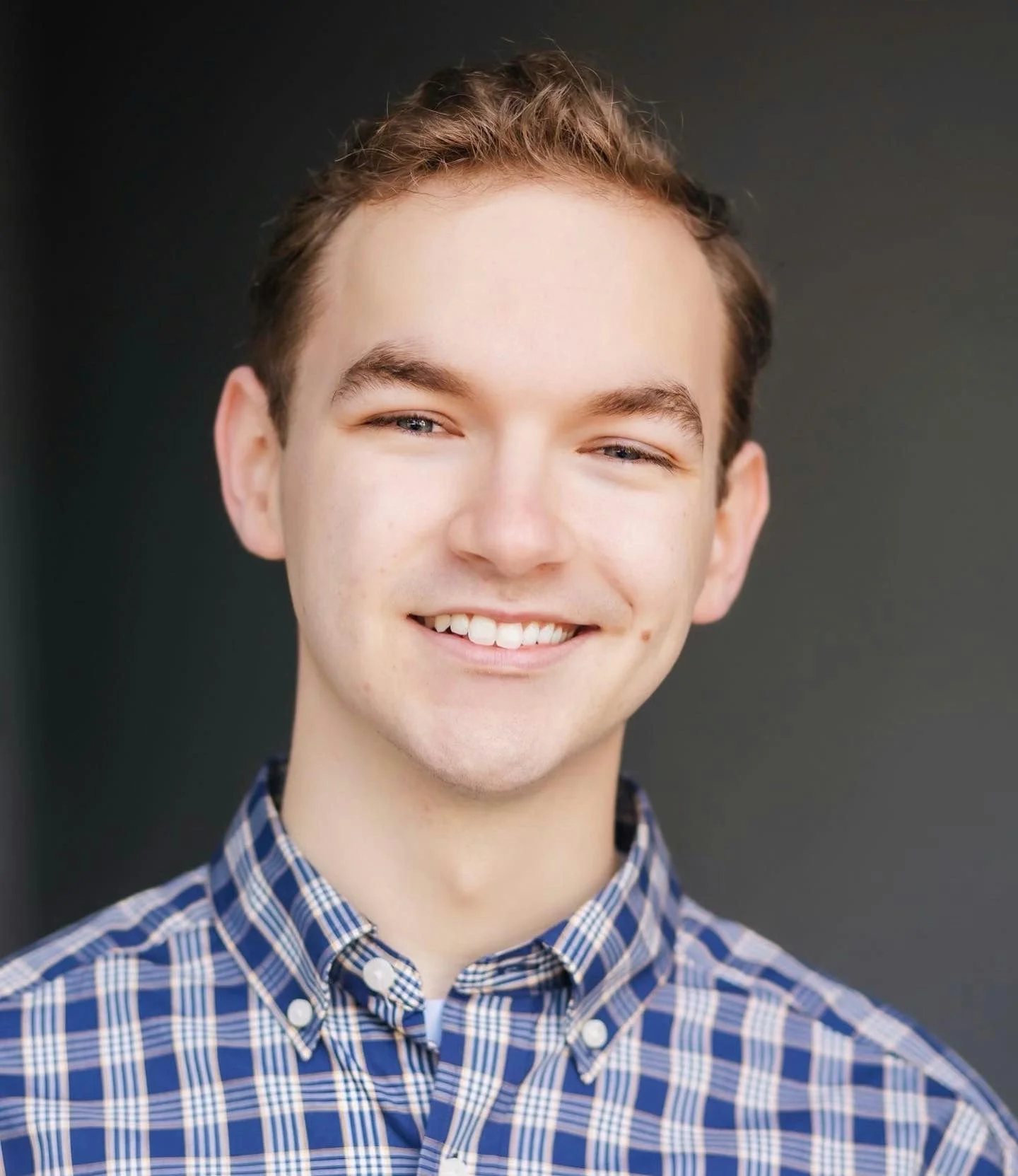 A woman with a buzz cut hairstyle, blue eyes, wearing earrings and a pink sleeveless top, looking directly at the camera with a neutral expression.
