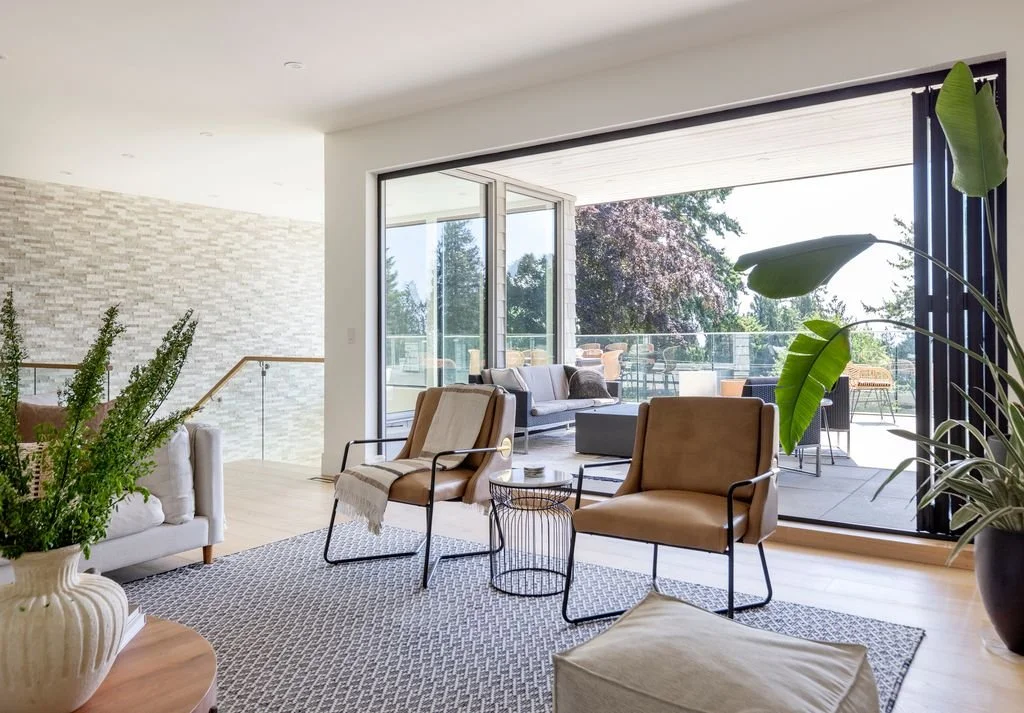 Modern living room with large sliding glass doors leading to a balcony with outdoor seating and trees in the background.