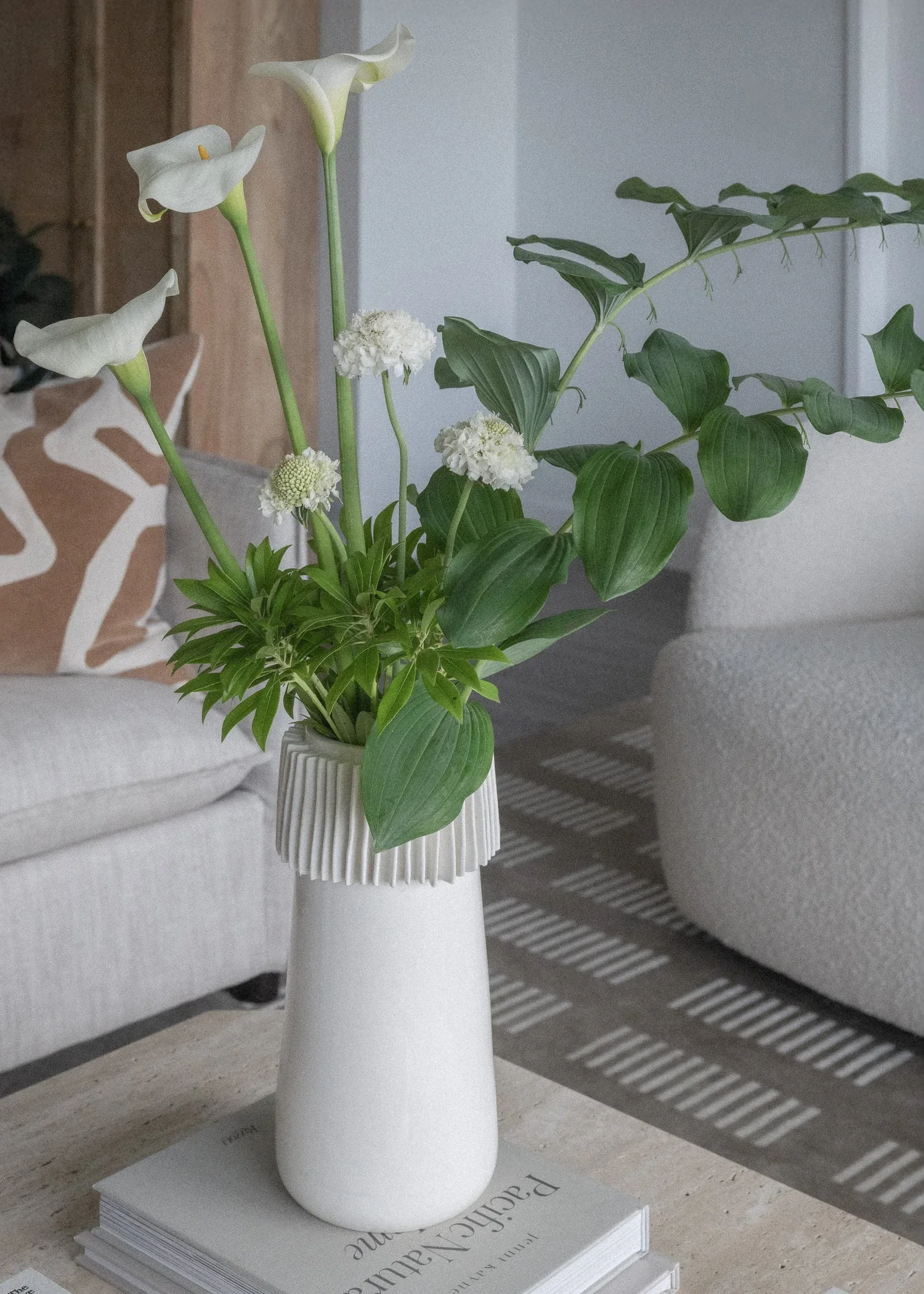 A white ceramic vase with calla lillies, solomons seal, and white scabious in a living room by Karla Dreyer.