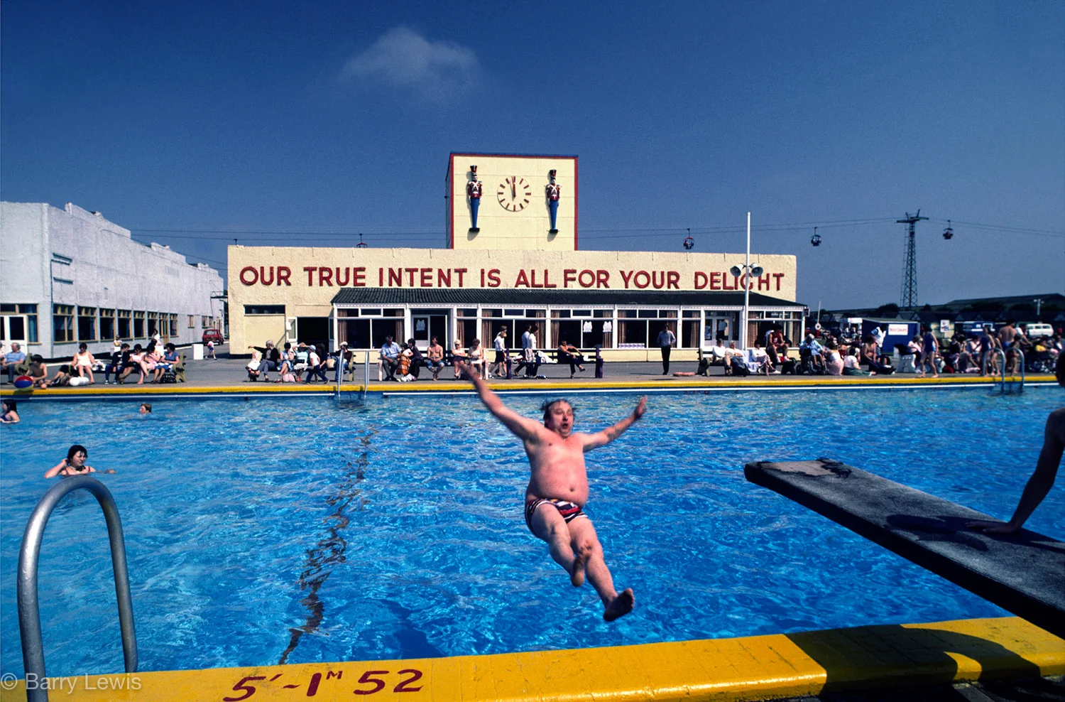 Man falling into swimming pool in Butlins holiday camp, Skegness, UK, 1982. The slogan 'Our true intent is all for your delight'. was borrowed by Billy Butlin from Shakespere's play, A Midsummer Night's Dream.