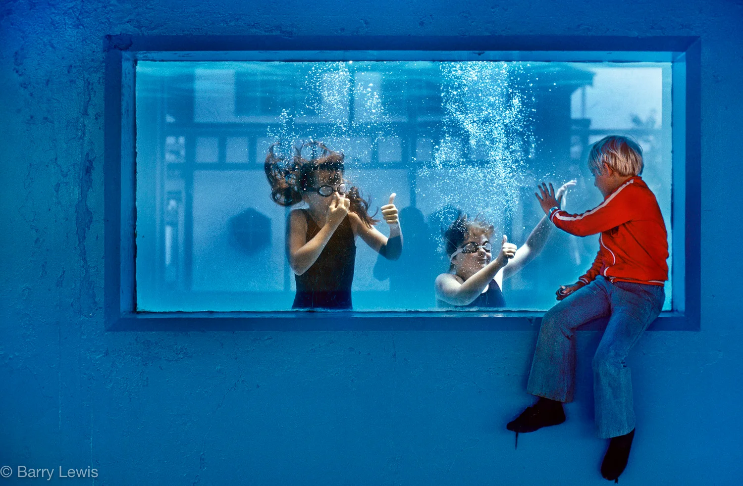 Boy watching the underwater swimmers through the swimming pool window. Butlins Holiday camp, Skegness UK 1982