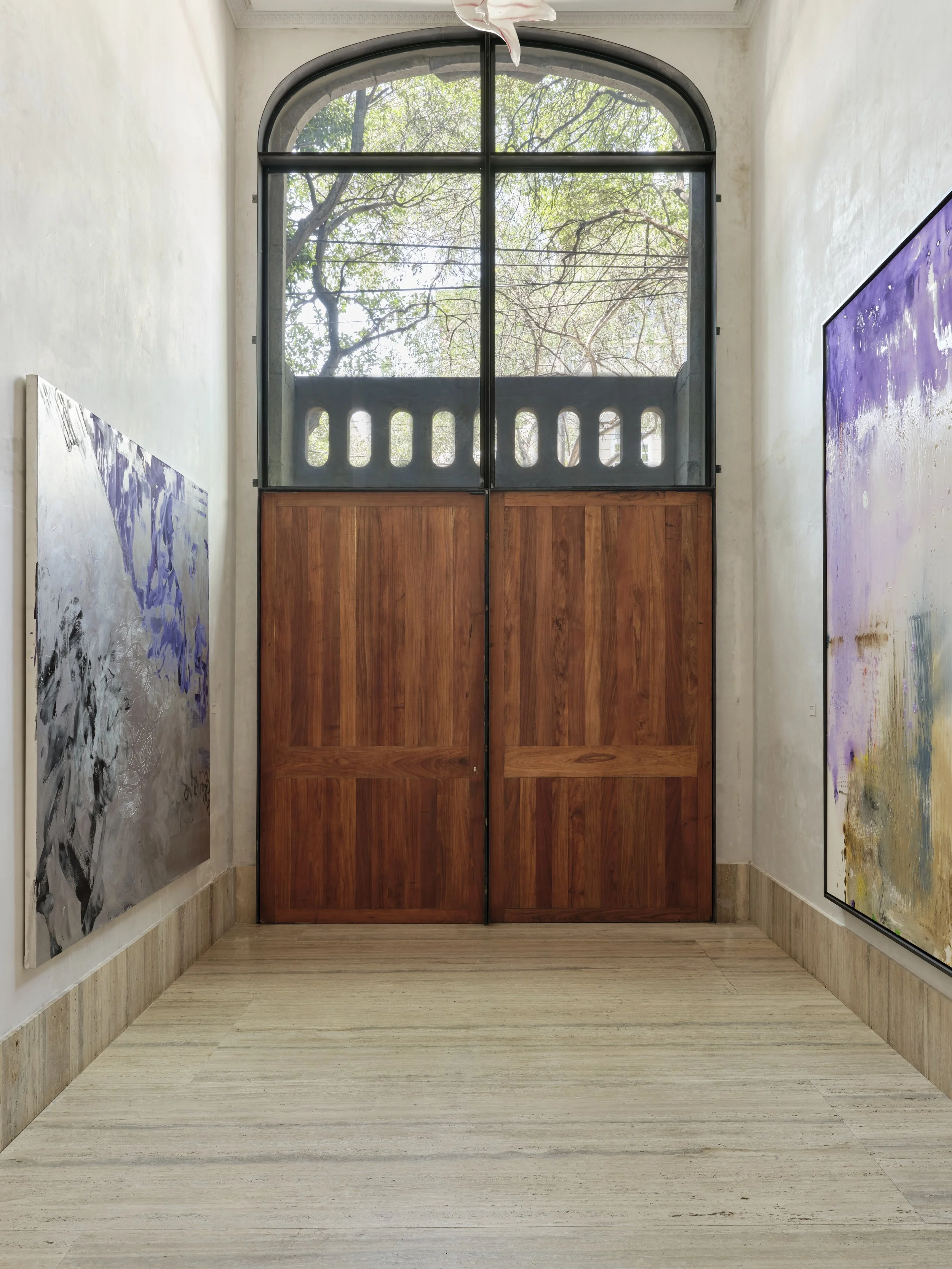 Gallery with two paintings on the walls and a large arched window showing trees outside.