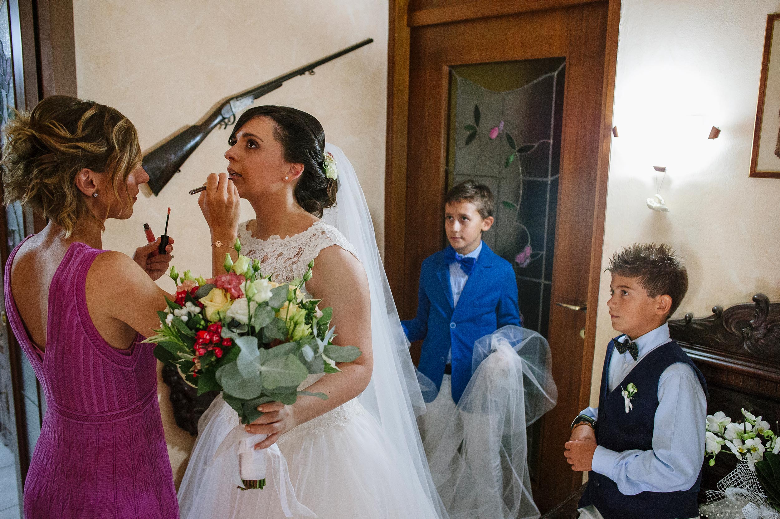bride-doing-last-make-up-retouches-rifle-on-the-wall-kids-holding-the-veil.jpg
