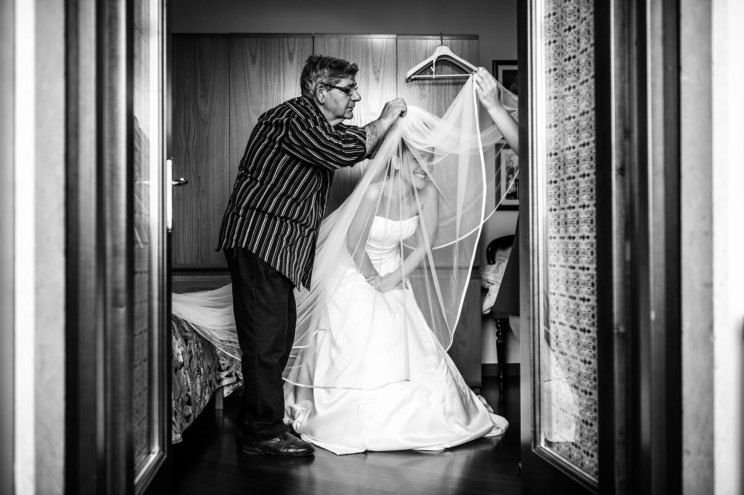bride-getting-ready-helped-by-a-man-putting-the-veil-on-black-and-white-wedding-photography.jpg