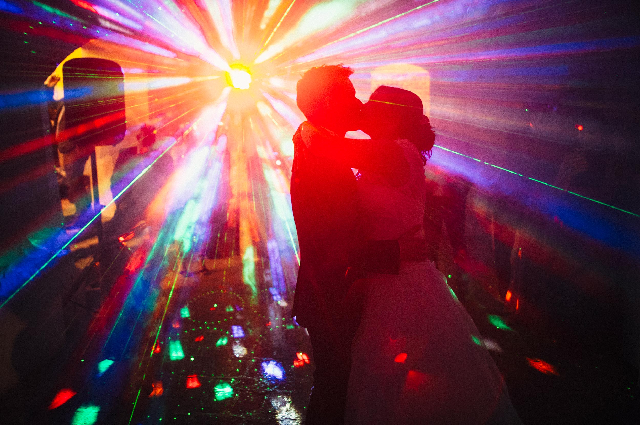 dj-lights-color-flare-strikes-on-the-dancefloor-while-bride-and-groom-kiss-during-the-first-dance-at-wedding.jpg