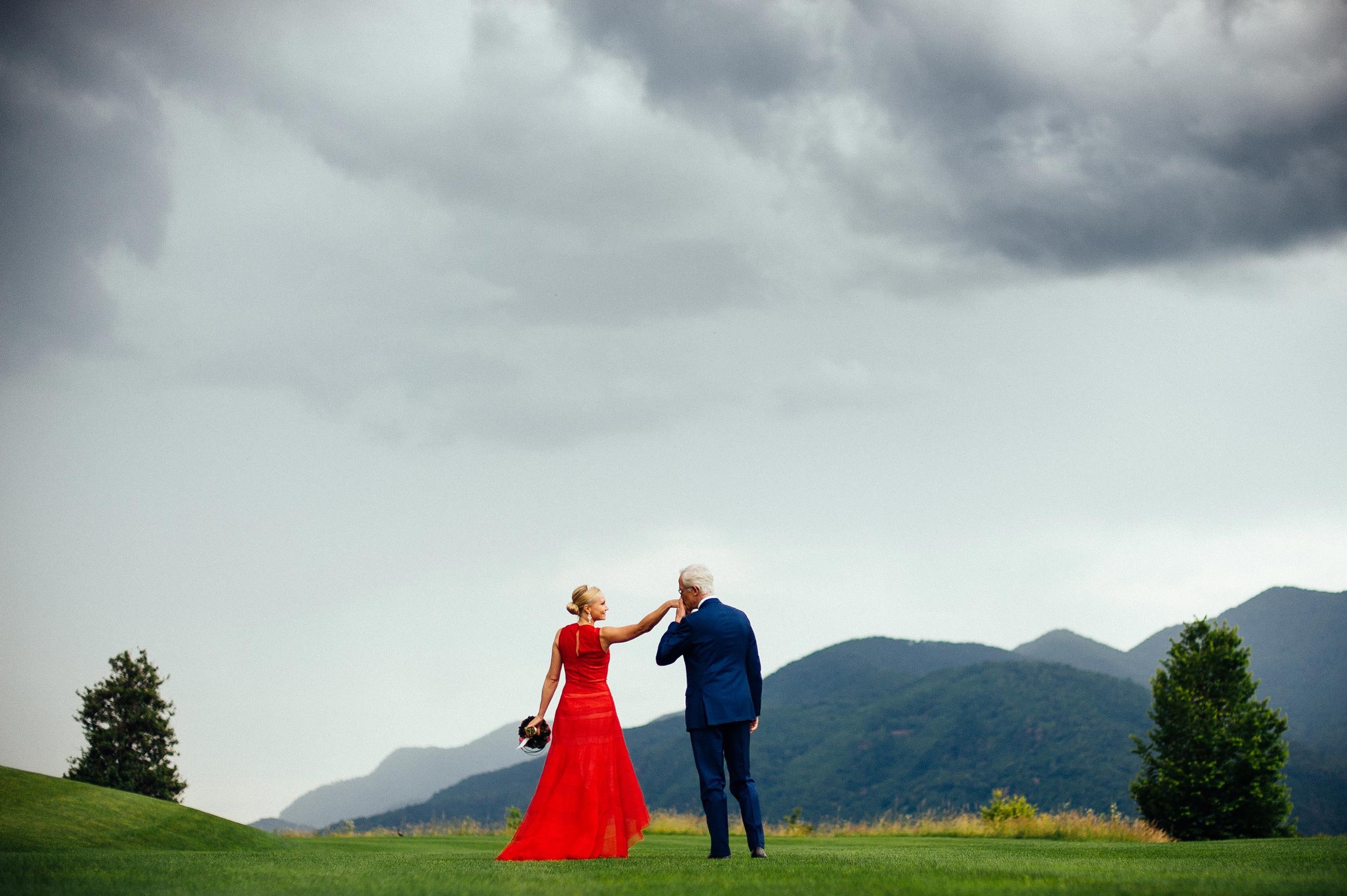 groom-in-blue-kisses-the-bride-with-red-wedding-dress-on-a-green-grass-field-lugano-switzerland.jpg