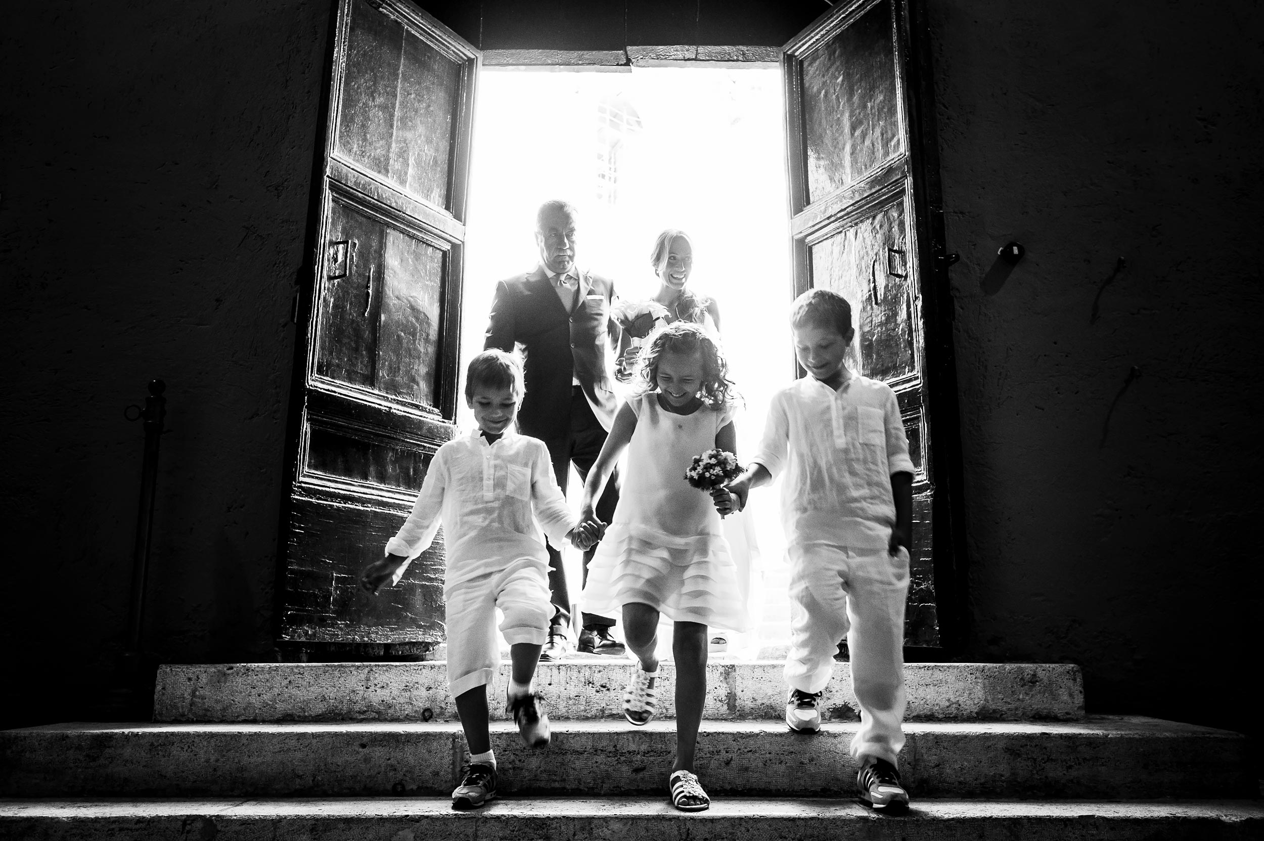 bride-and-dad-enter-church-with-three-kids-down-the-steps-vatica-city-rome-black-and-white-wedding-photography.jpg