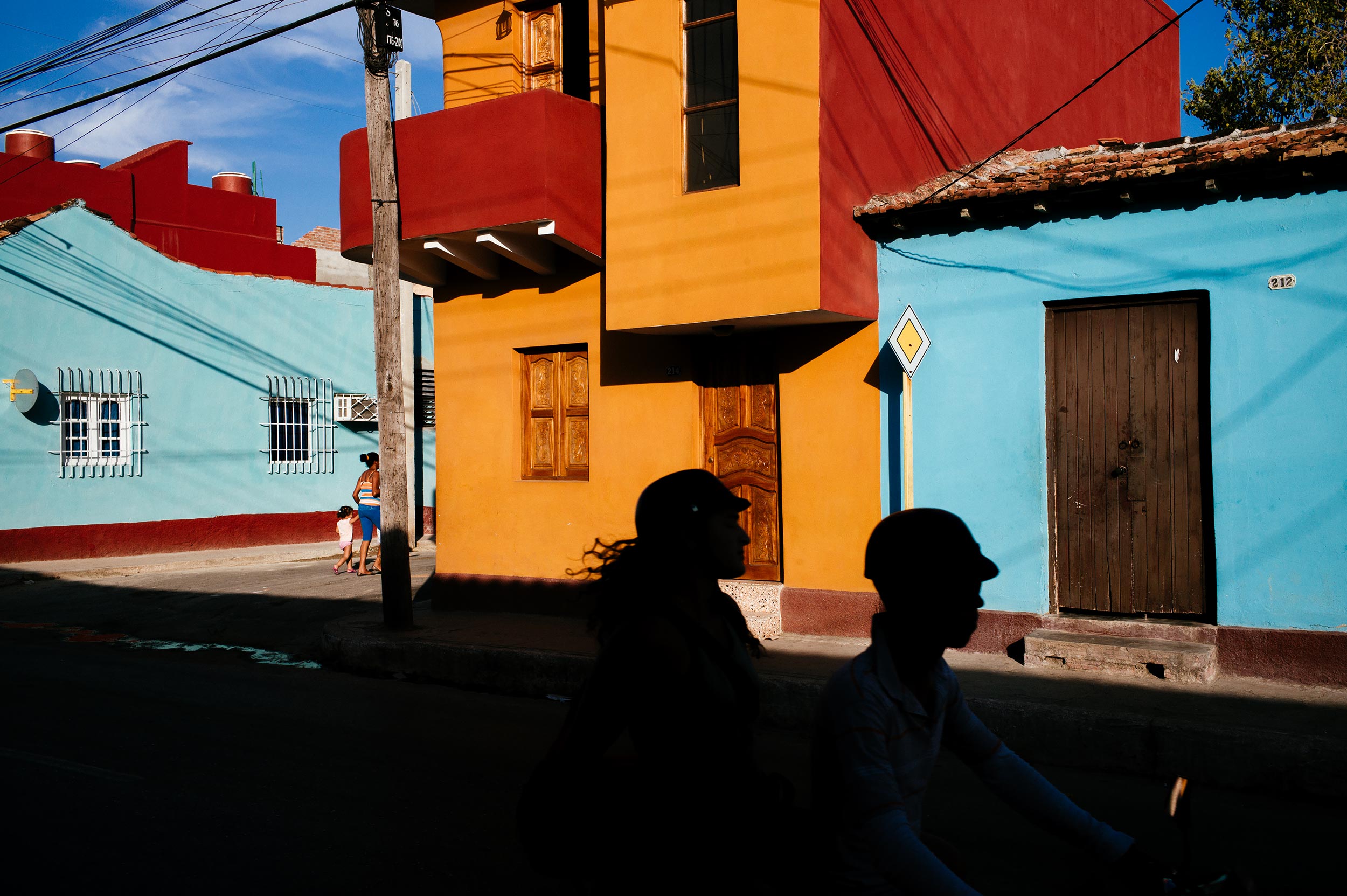 Trinidad-2016-scooter-passes-in-front-of-coloured-houses-while-woman-walks-with-small-daughter-street-photography-by-Alessandro-Avenali.jpg