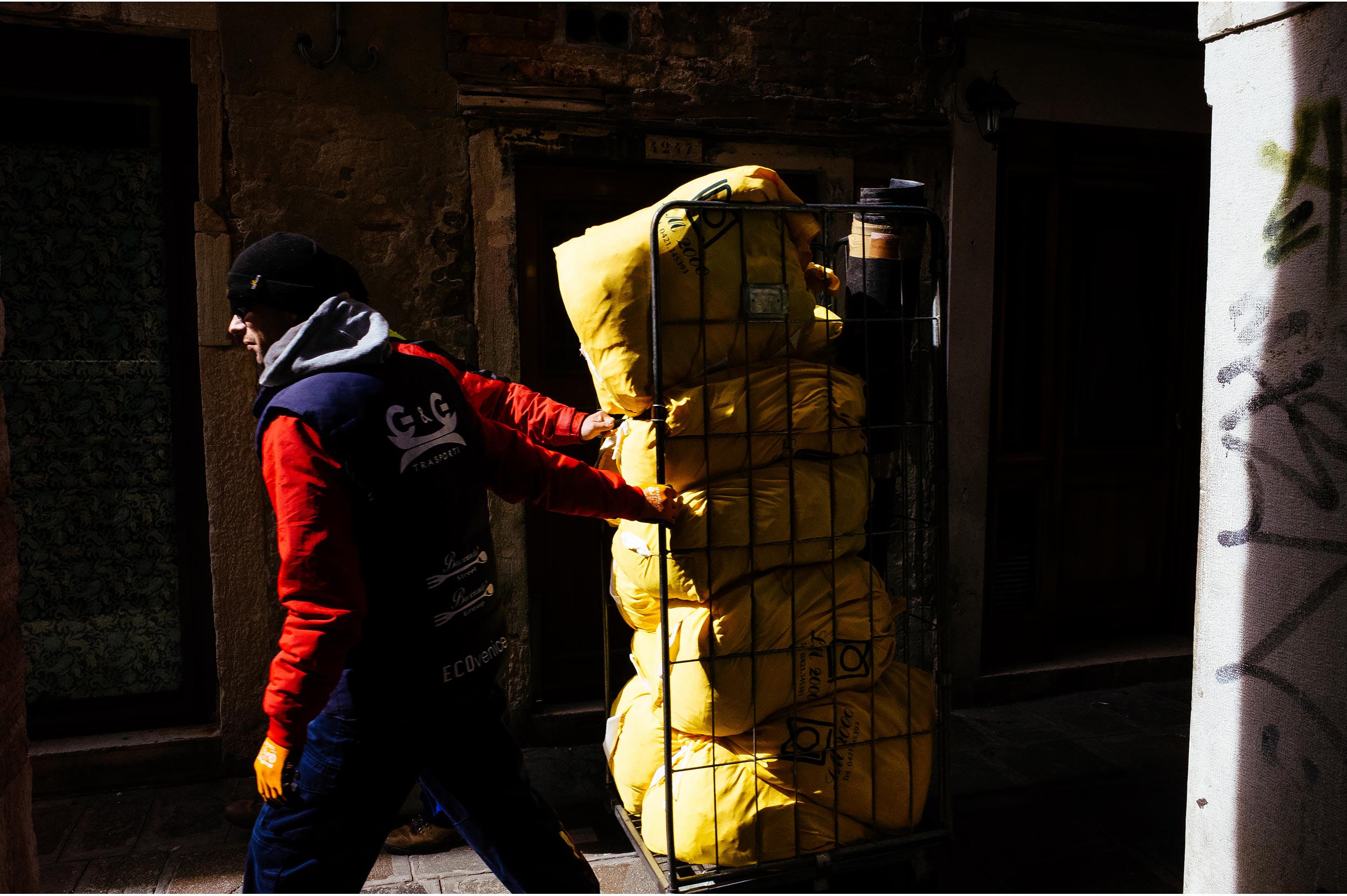 Venice, Italy, 2016. Two workers carrying some stuff look like one having three arms.