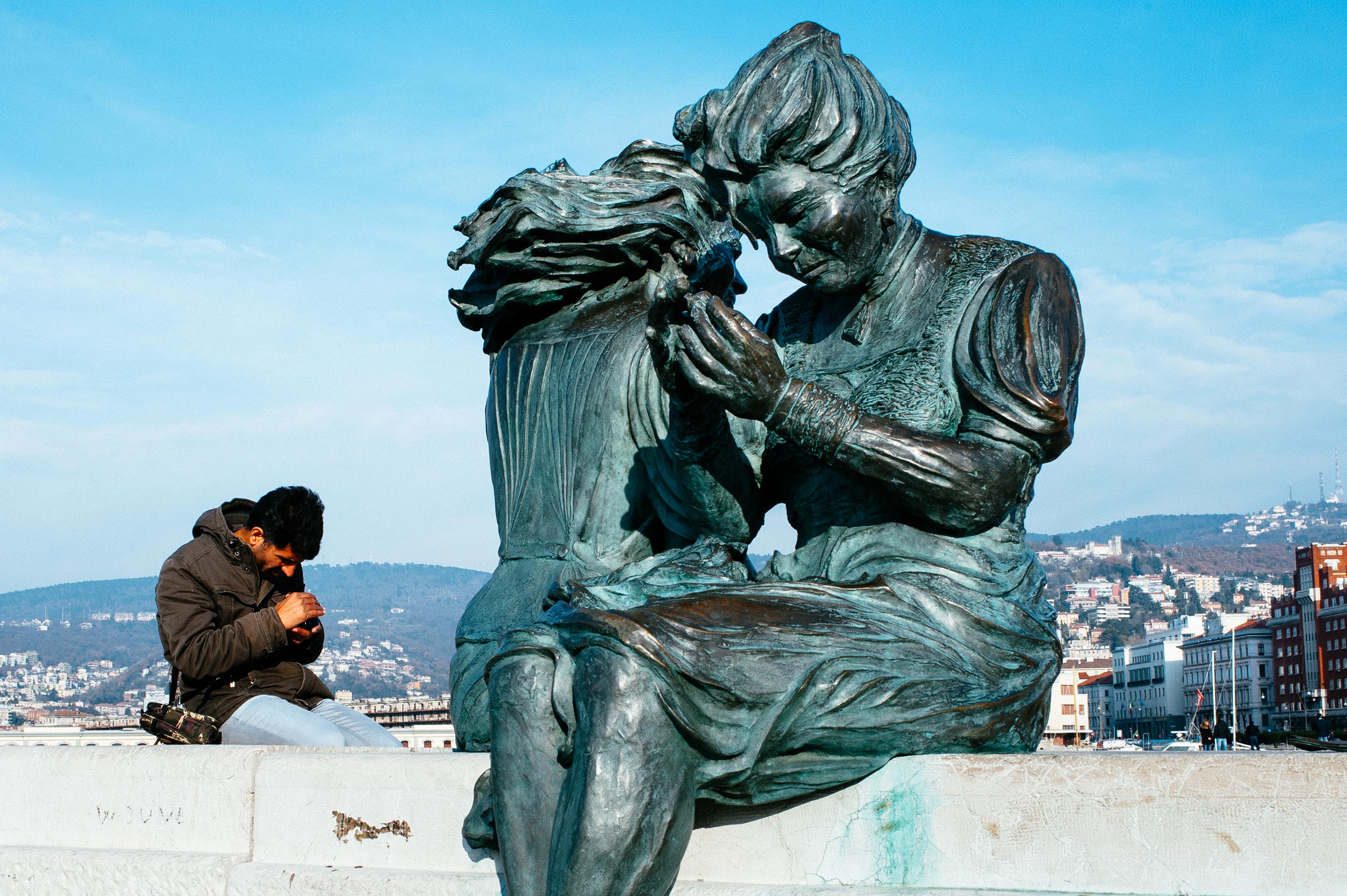 Trieste, Italy, 2015. A man looking at his smartphone has the same pose as a bronze statue near him.