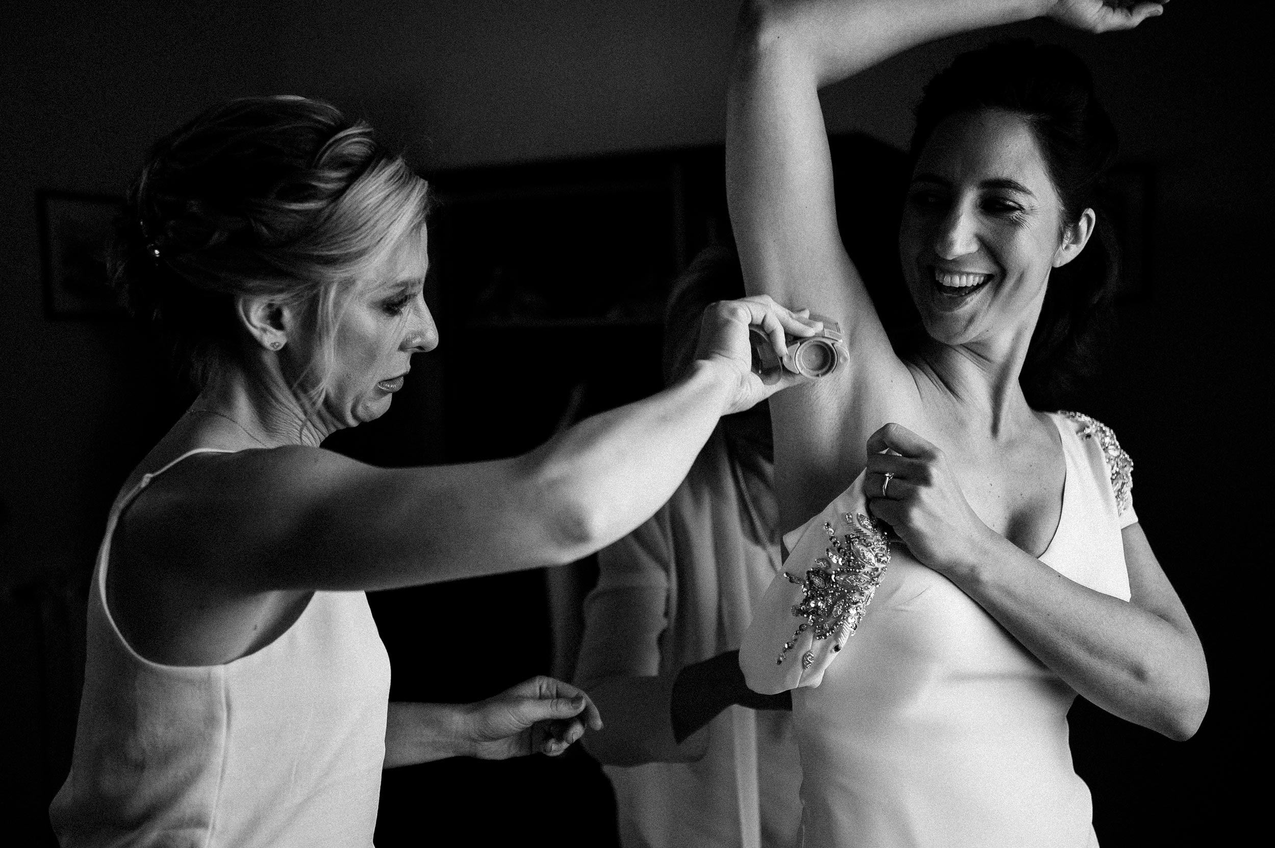 Bride getting ready with her friend putting deodorant stick on. Candid wedding photos.