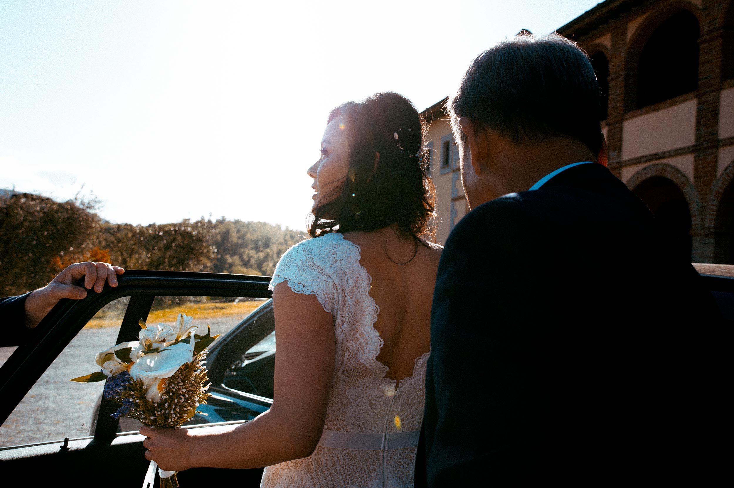American Korean bride enters the car while looking at the Ceremony place Tuscany Wedding in Siena by Alessandro Avenali