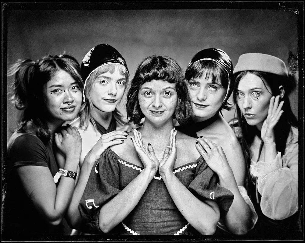 The band Gelli Haha, five of them posed close together on one plate with their hands raised beside their faces. Wet plate collodion tintype.