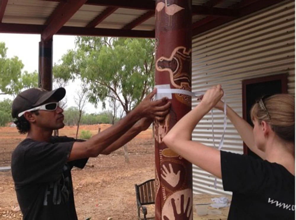 Sophie and Kenny, an arts centre employee, work together to re-adhere delaminating paint flakes to the outdoor wooden pole / Photograph by Jenny O’Connell