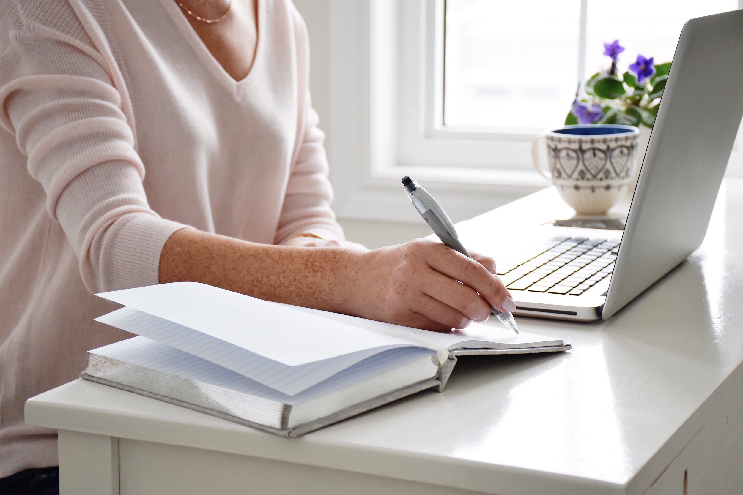 woman-is-sitting-at-a-desk-in-an-office-in-front-of-a-laptop-computer-and-writing-notes-in-a-notebook_t20_znwG8G.jpg
